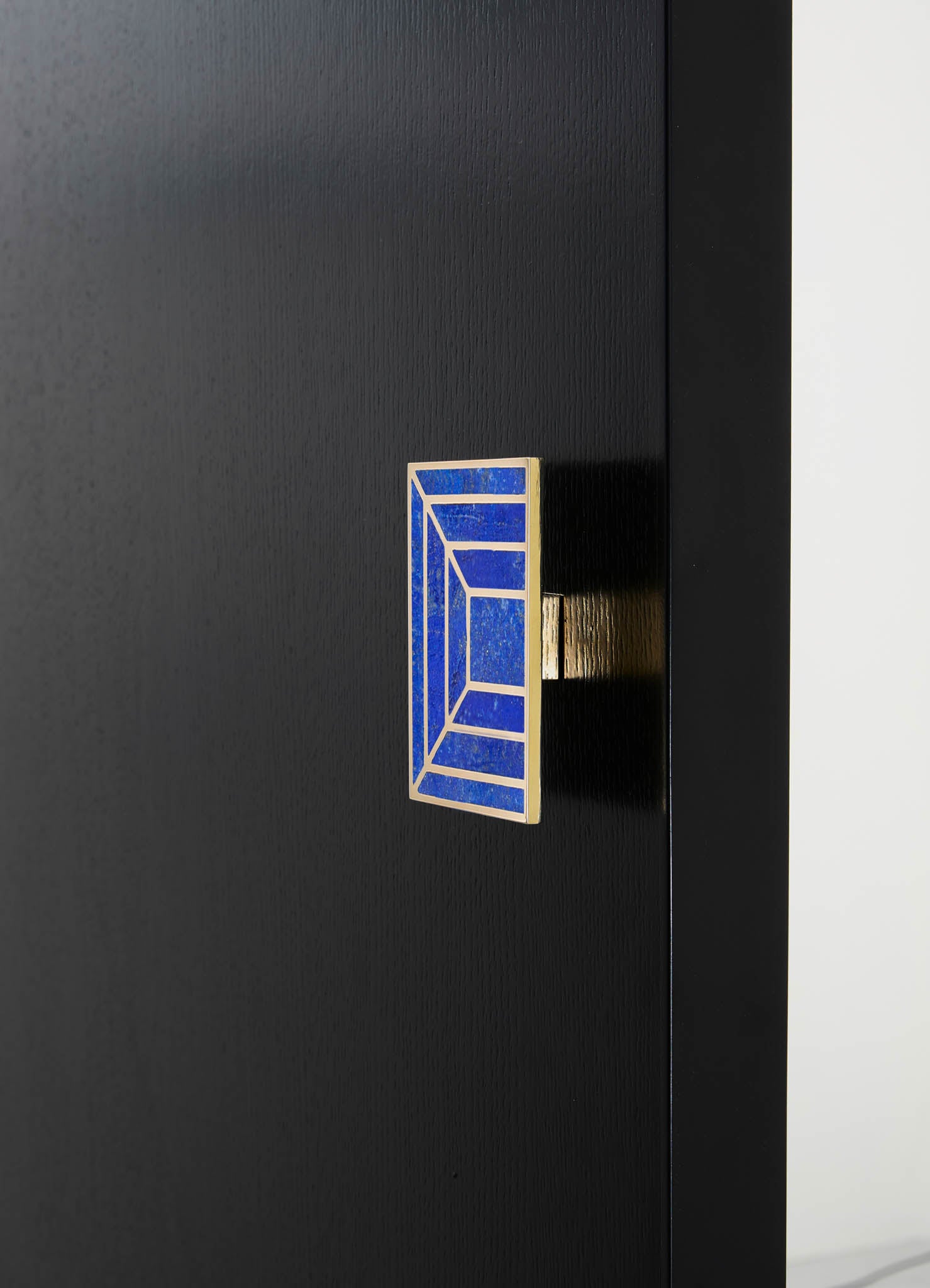 Close-up of a black wood cabinet with a geometric tile handle in blue and white with metallic accents, highlighting a modern, minimalist design.