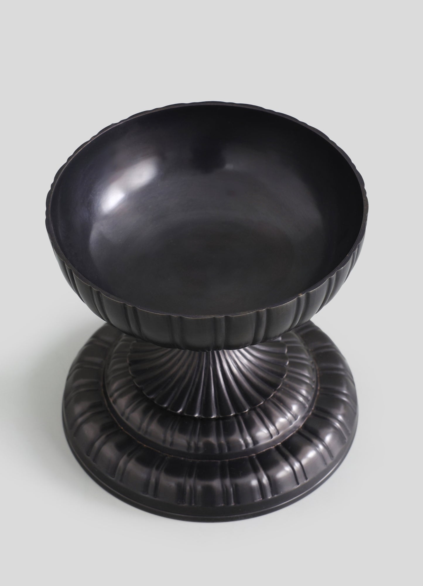 Black ceramic bowl with a fluted exterior and smooth interior, mounted on a matching fluted pedestal base.