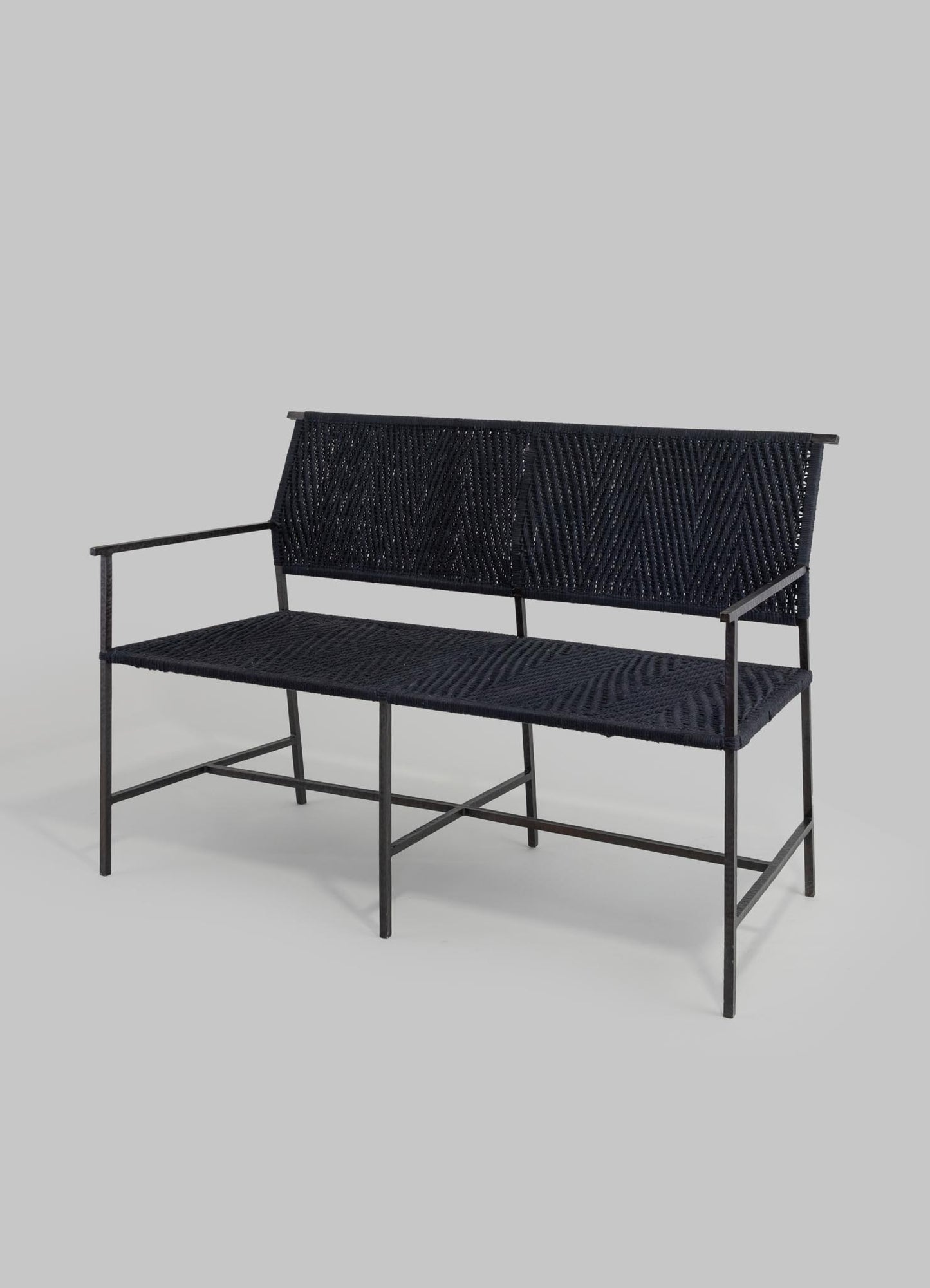 Woven black metal bench with a minimalist frame and a textured woven seat and backrest, featuring slim armrests and an open design in a contemporary style.