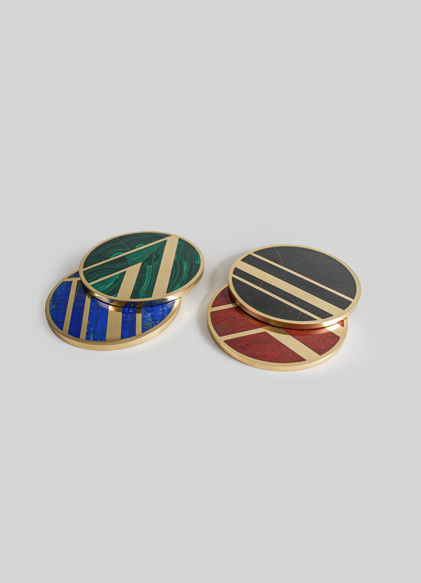 Set of four round coasters with geometric patterns in bold colors including green, blue, black, and red, framed with gold borders, on a plain light gray background.
