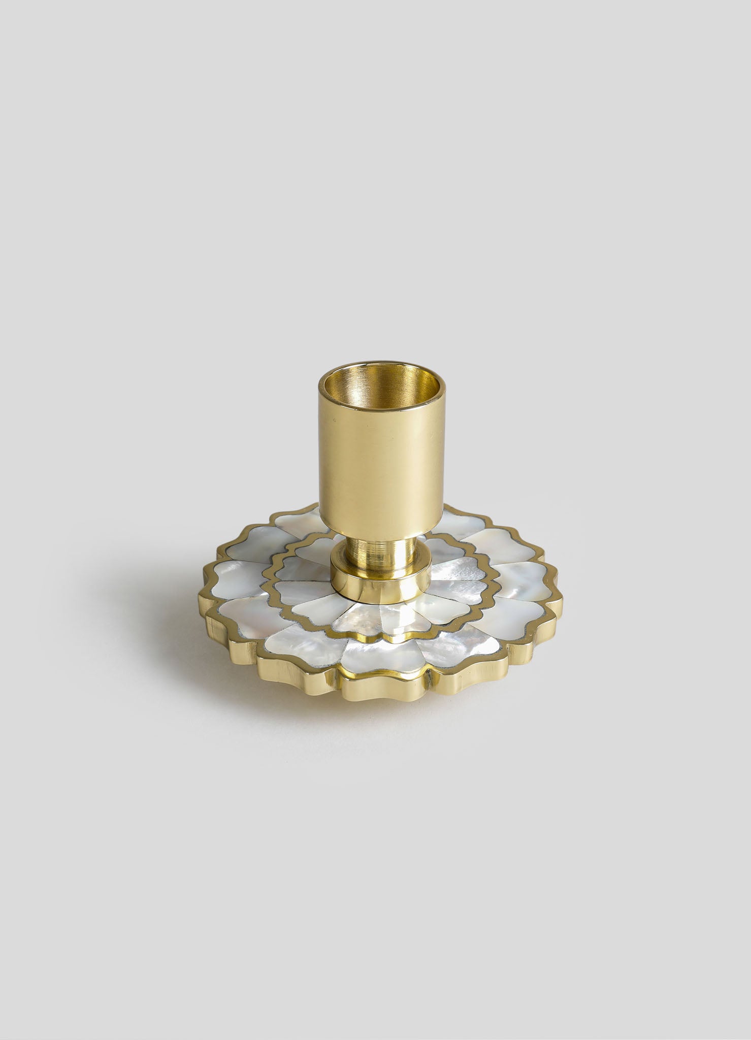 A brass candle holder with a cylindrical cup and a mother-of-pearl decorative base in scalloped, layered patterns, presenting a luxurious and ornate style.