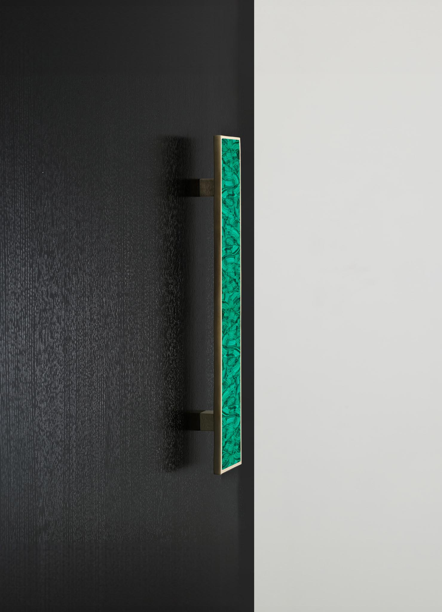 A modern wall sconce with a rectangular glass panel featuring a swirling green pattern, framed in a light-colored material. The fixture is mounted on a black wall with a white background visible nearby.