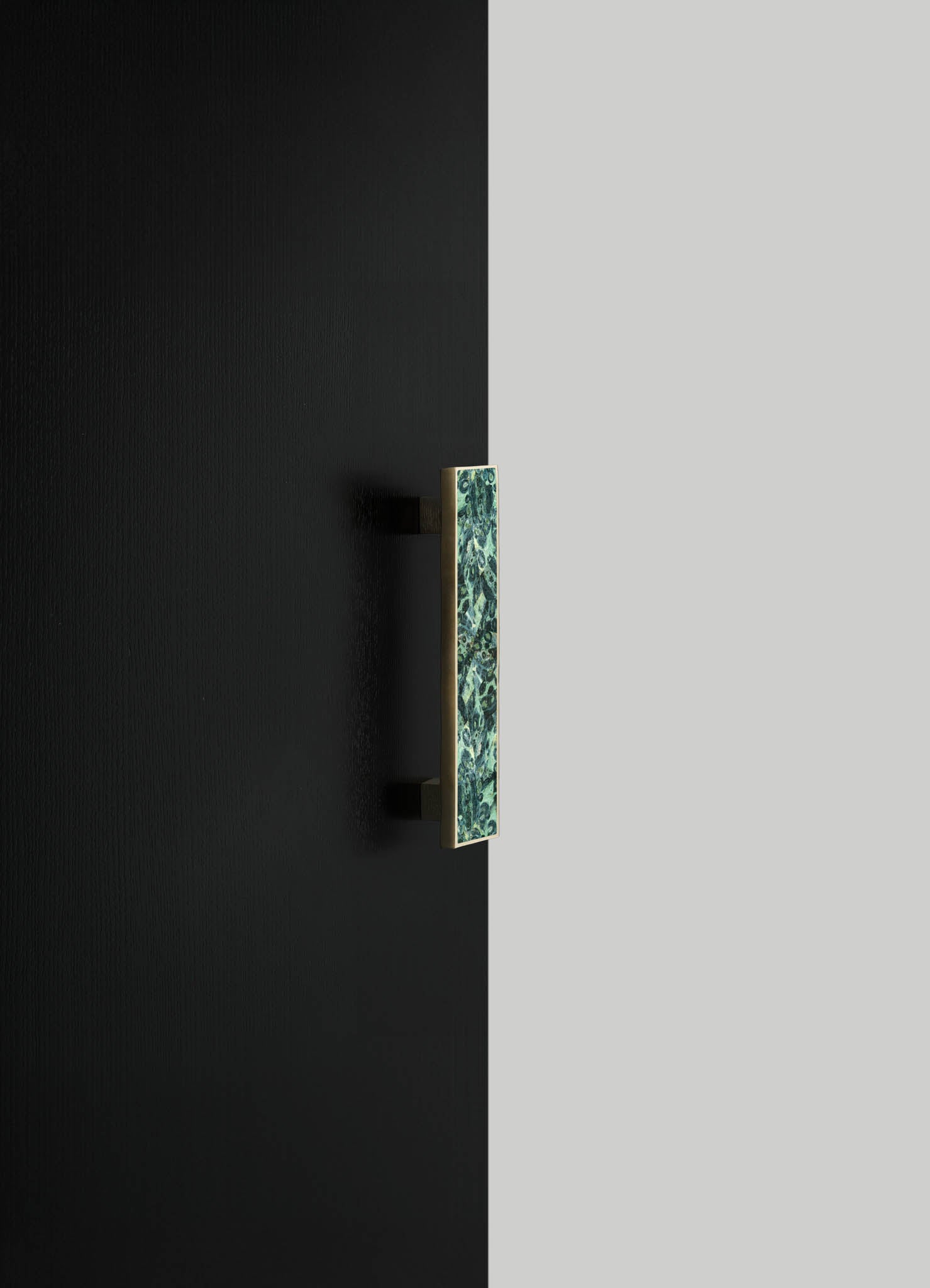 A wall-mounted light fixture with a rectangular ceramic shade displaying a blue and green floral motif, set against a black and gray split wall background. The fixture has a metal arm and base with a matte finish, blending contemporary and decorative styles.