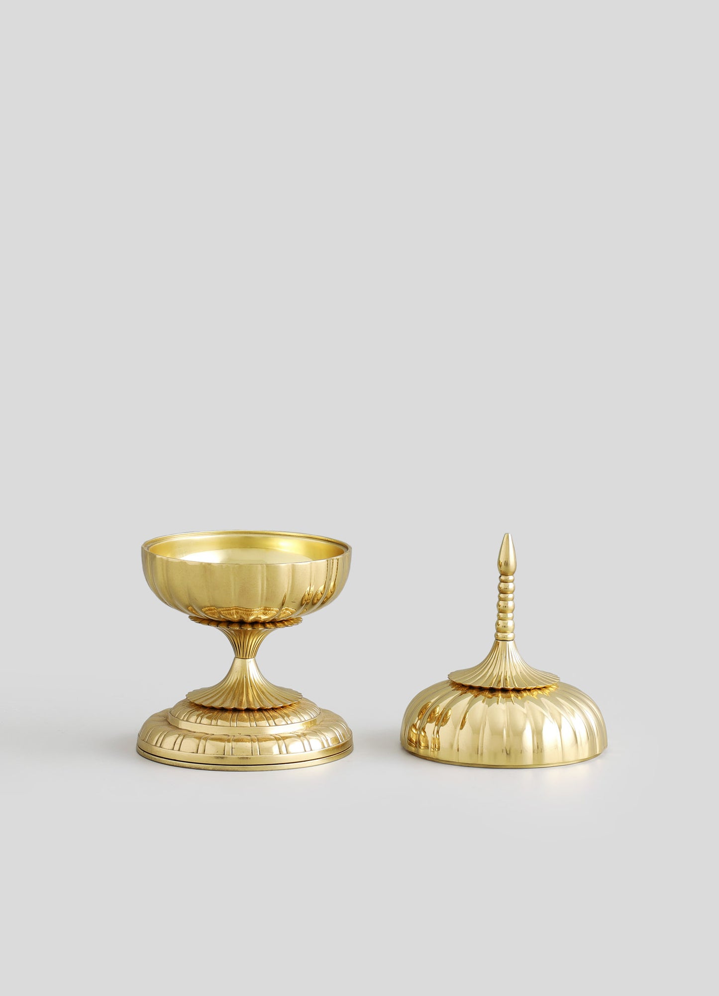 Gold-plated decorative bowls with ribbed and fluted motifs, one with a shallow, rounded shape and the other with a pointed lid and finial, featuring a shiny metallic finish.