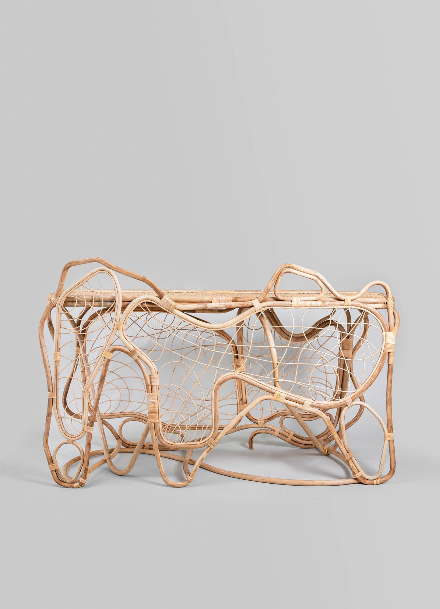 A woven rattan coffee table with an organic, freeform design featuring intricate web-like patterns and natural wood tones, set against a plain background.