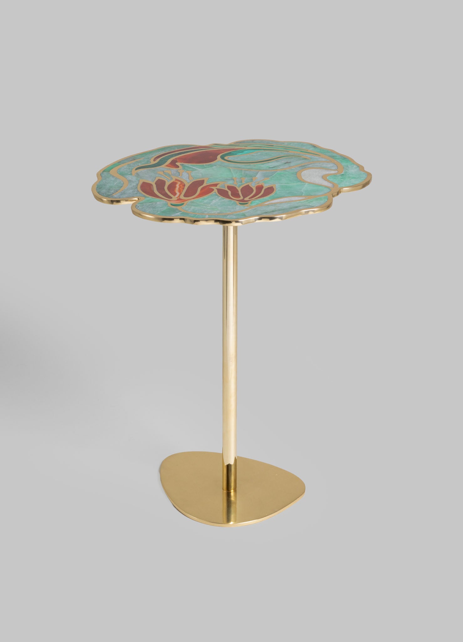 A side table with a brass base and a scalloped-edge top featuring a floral motif in shades of red, green, and cream, made from a material resembling ceramic or enamel. The design has an elegant, contemporary style with handcrafted detailing.
