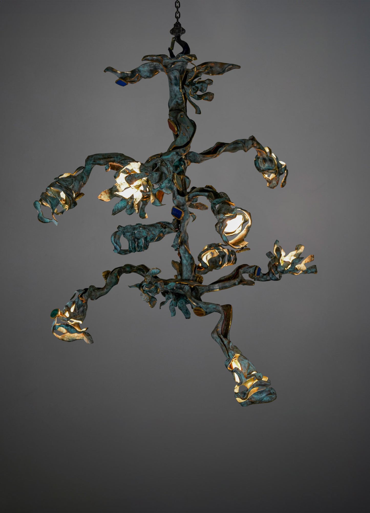 A chandelier with an organic, sculptural design made of metal with a weathered, patina finish. It features irregular, twisting arms and exposed bulb sockets, creating a contemporary and artistic lighting fixture.