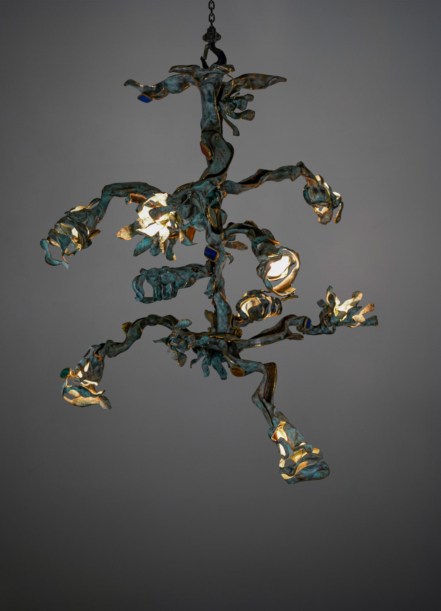 A chandelier with an organic, sculptural design made of metal with a weathered, patina finish. It features irregular, twisting arms and exposed bulb sockets, creating a contemporary and artistic lighting fixture.