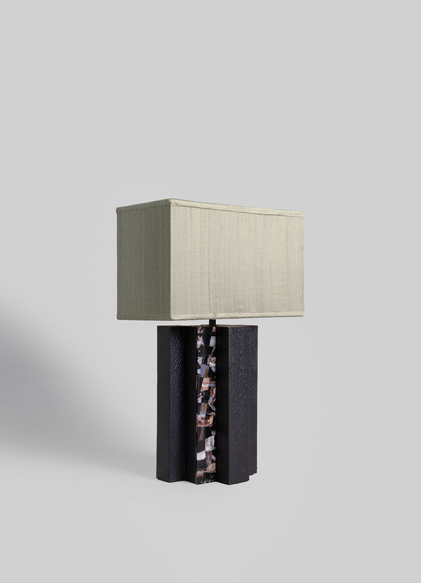 Table lamp with a rectangular off-white fabric shade and a black wooden base featuring a textured and mottled pattern, set against a plain background.