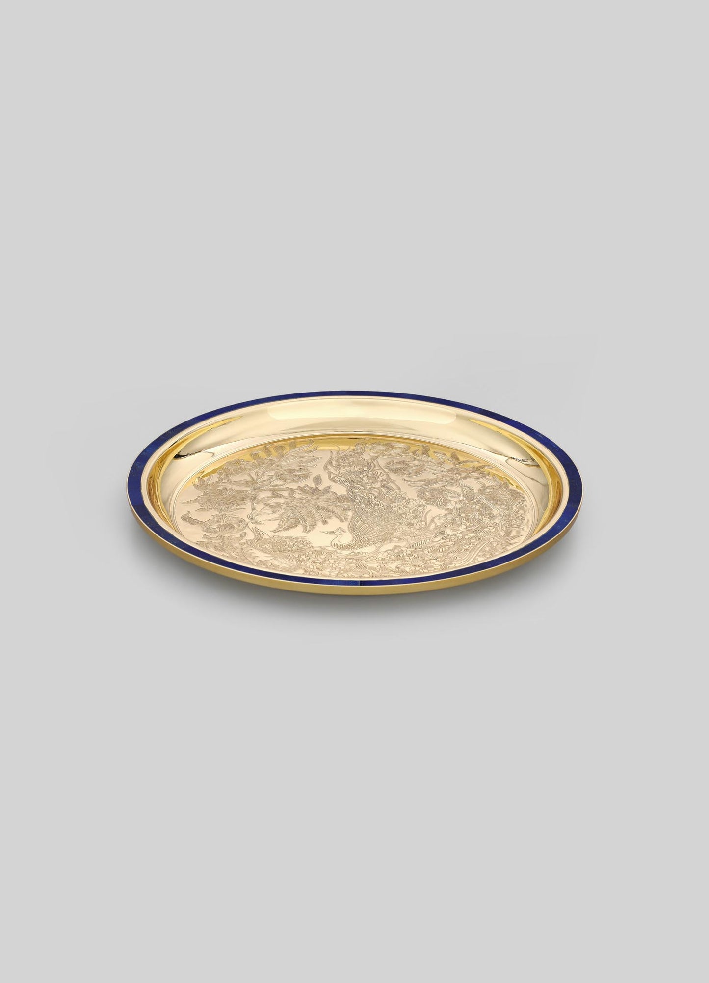 A round decorative tray with a gold metallic finish, featuring intricate engraved motifs and a dark-colored rim.