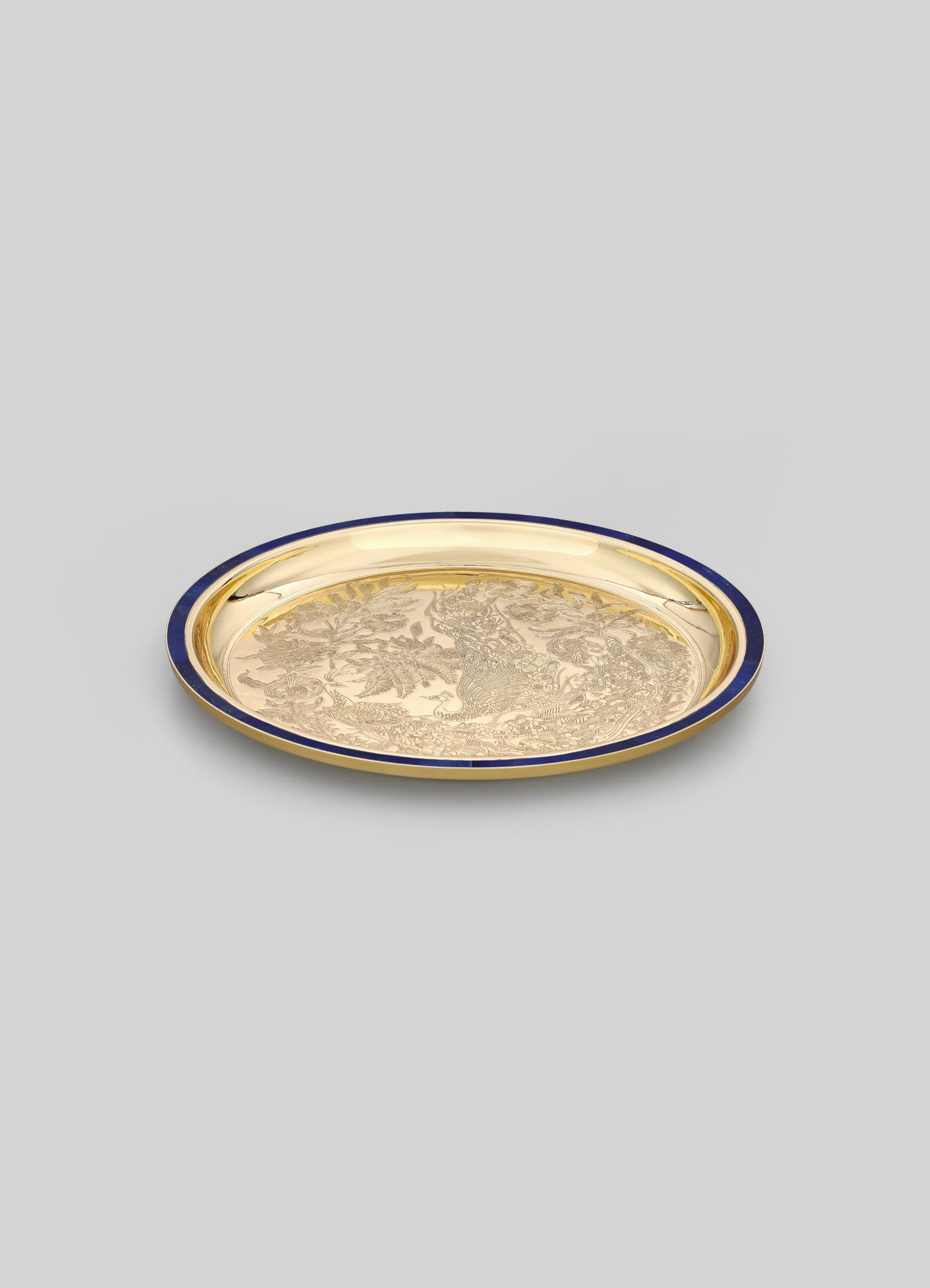A round decorative tray with a gold metallic finish, featuring intricate engraved motifs and a dark-colored rim.