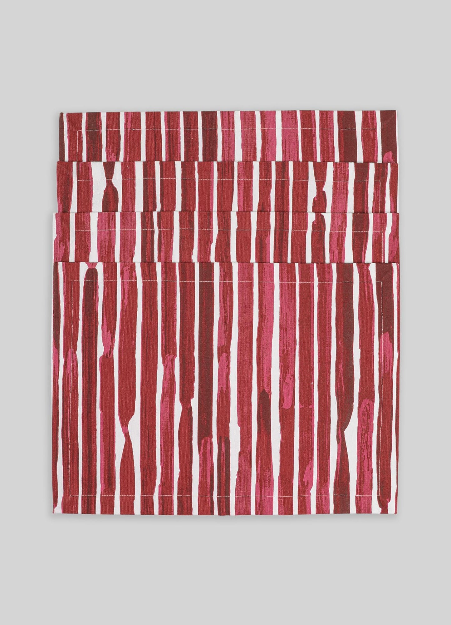 A folded textile piece featuring vertical stripe patterns in shades of red, pink, and white, with a textured appearance on a light gray background.