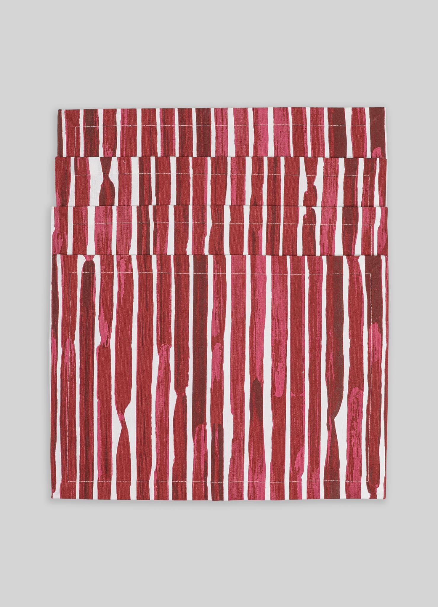 A folded textile piece featuring vertical stripe patterns in shades of red, pink, and white, with a textured appearance on a light gray background.