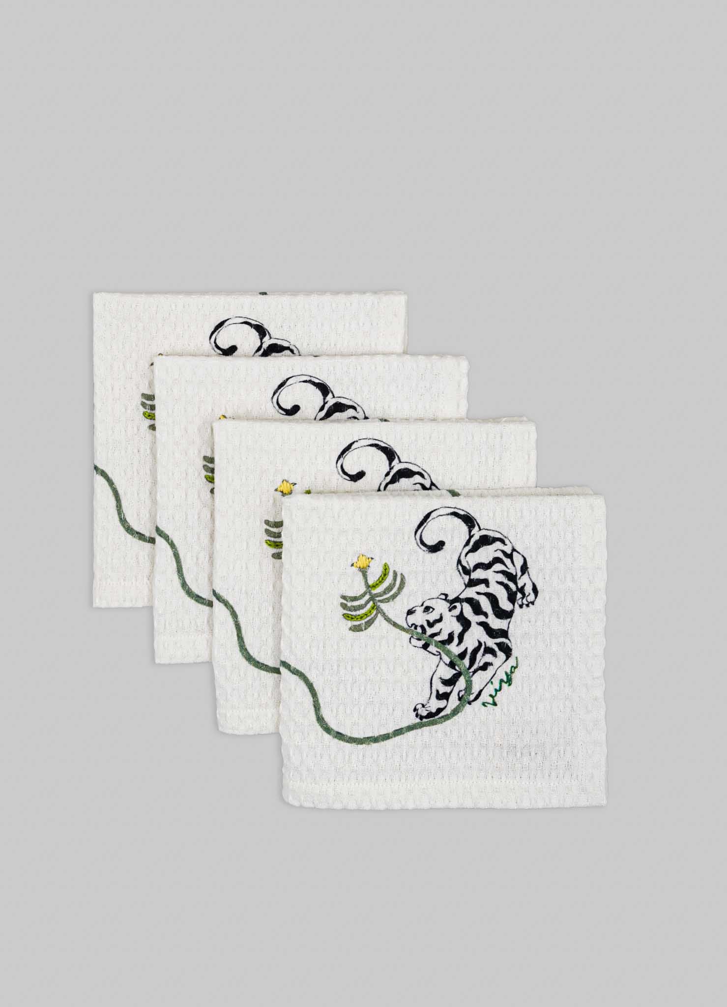 Set of four white fabric napkins with embroidered black and white tiger motifs and green and yellow floral accents, featuring a textured surface.