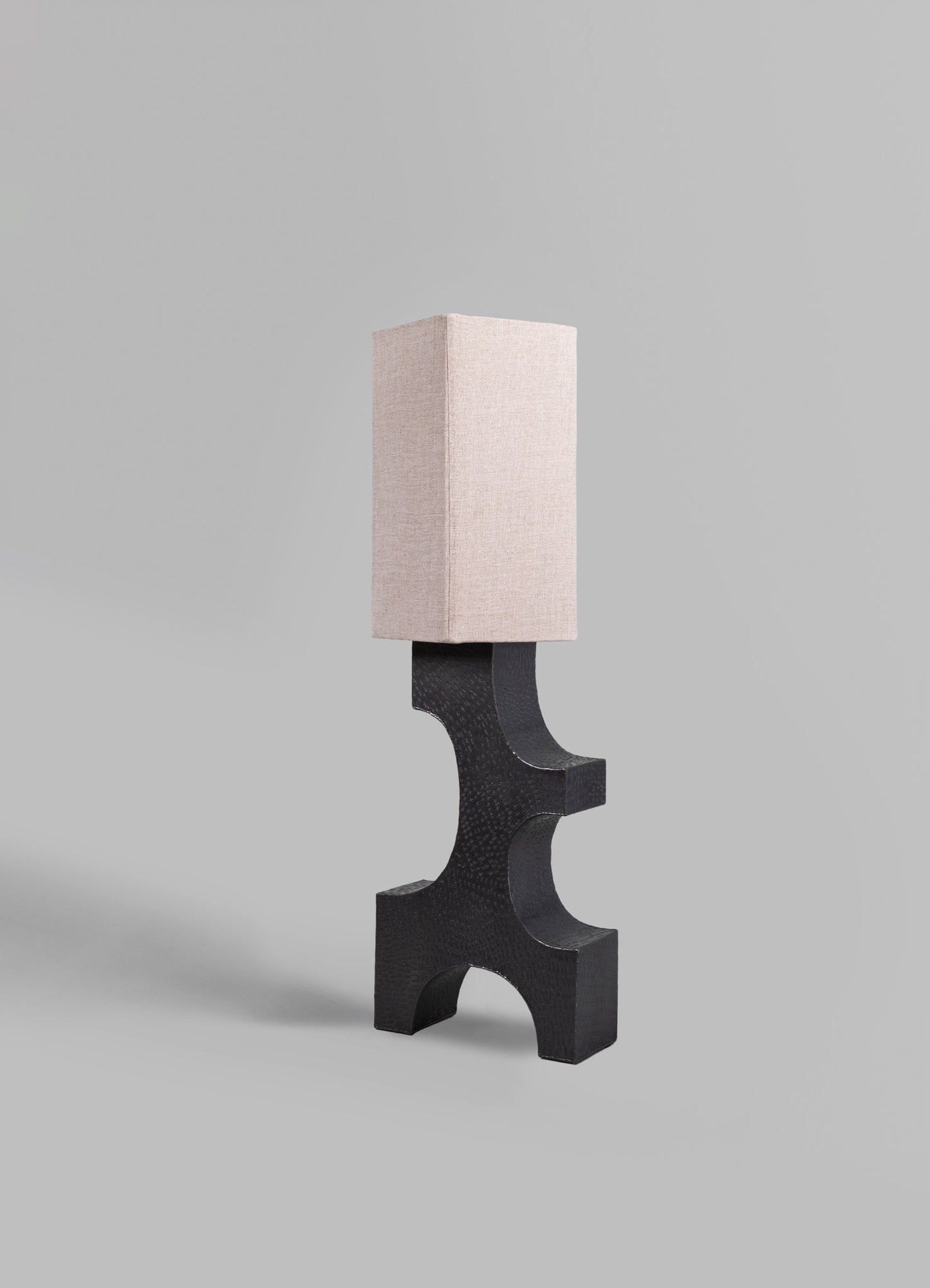 A modern table lamp featuring a rectangular beige fabric shade mounted on a sculptural black wood base with curved and geometric shapes.