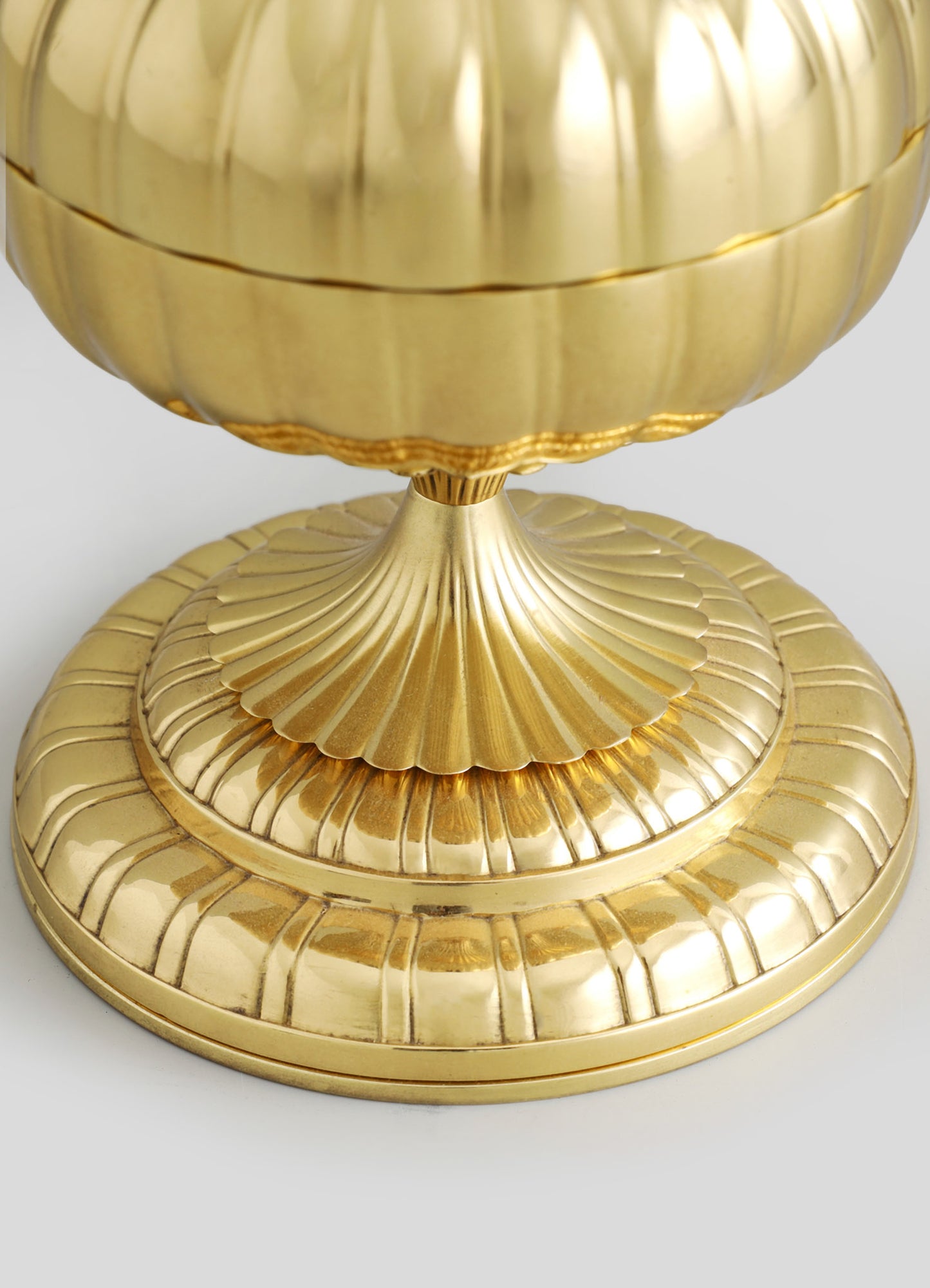 A decorative gold bowl with a fluted design, crafted from metal, sits on a matching round base with similar fluted detailing. The polished finish gives it a luxurious and contemporary appearance.