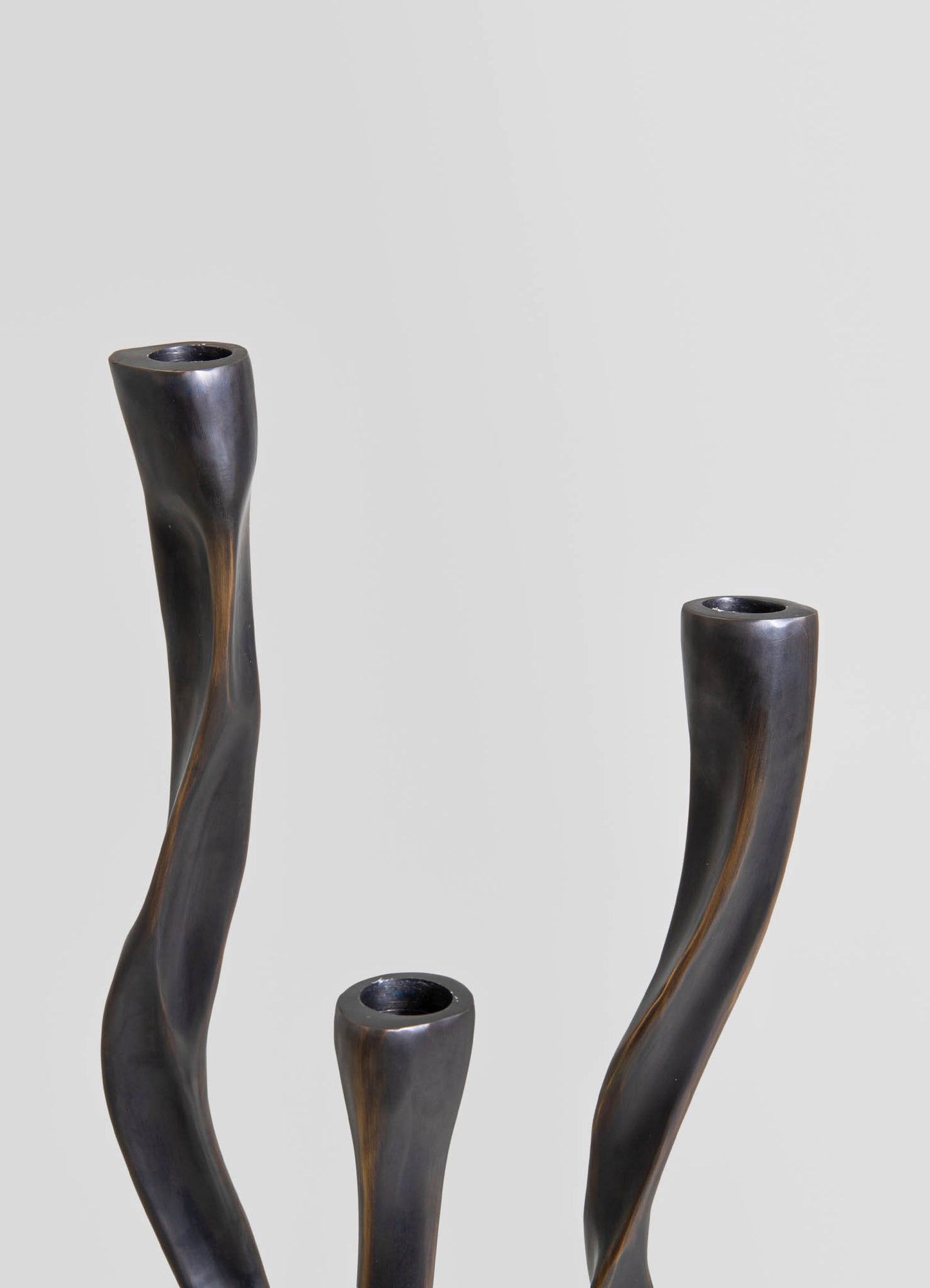 Metallic black and bronze vases with organic, twisted forms, made of smooth metal. The vases have cylindrical openings and a contemporary, sculptural style.