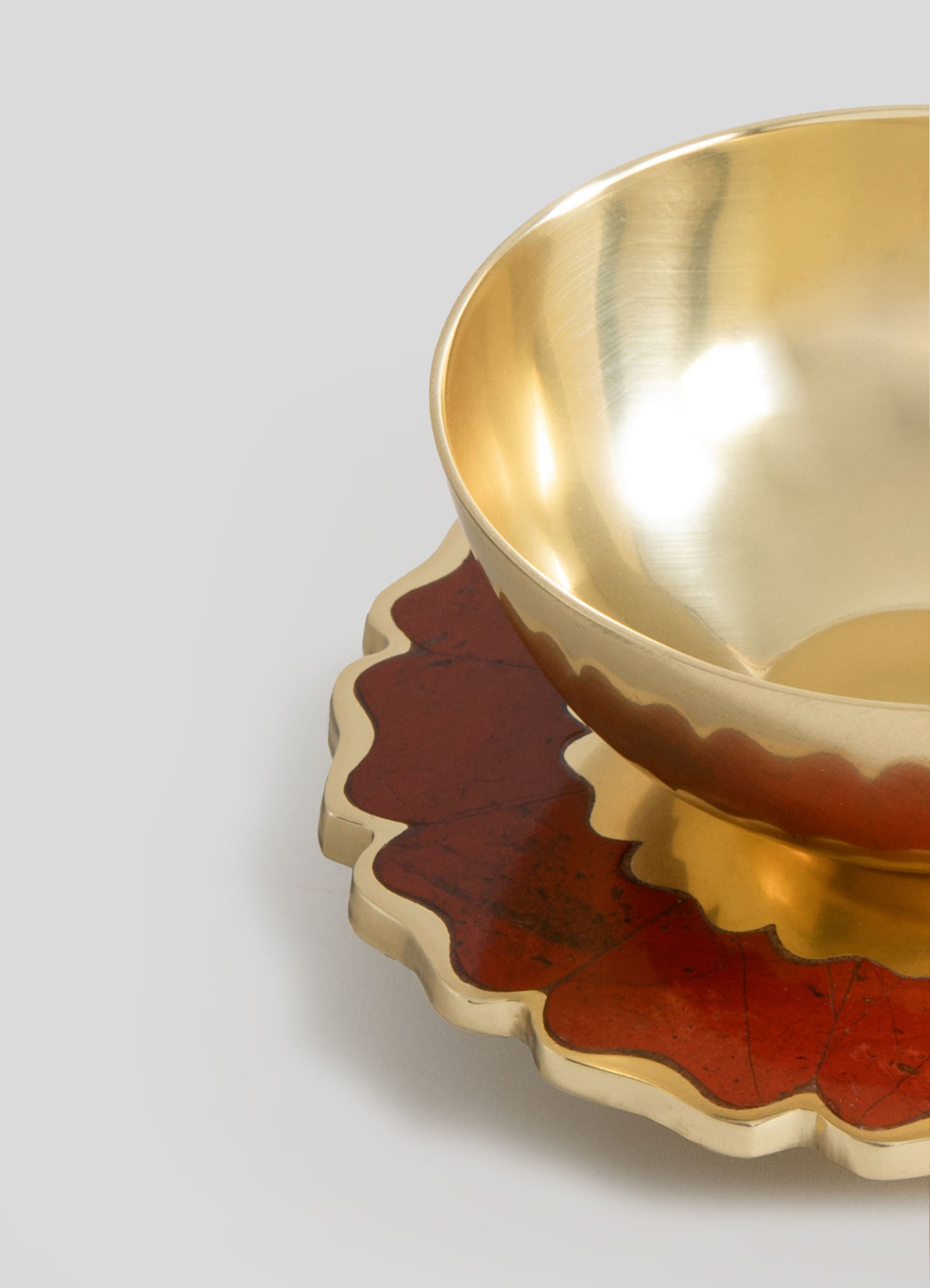 A decorative bowl with a smooth, reflective gold interior and a matte exterior in a warm, reddish-brown color with irregular, scalloped edges. The bowl rests on a matching scalloped tray or base, combining metallic and earthy materials.