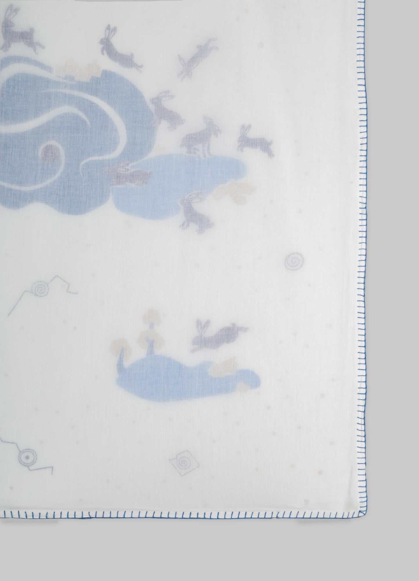 A fabric with a light background featuring a pattern of blue clouds and gray rabbits, bordered by a blue stitch edge. The material appears to be soft and lightweight, likely suitable for textiles or home decor.