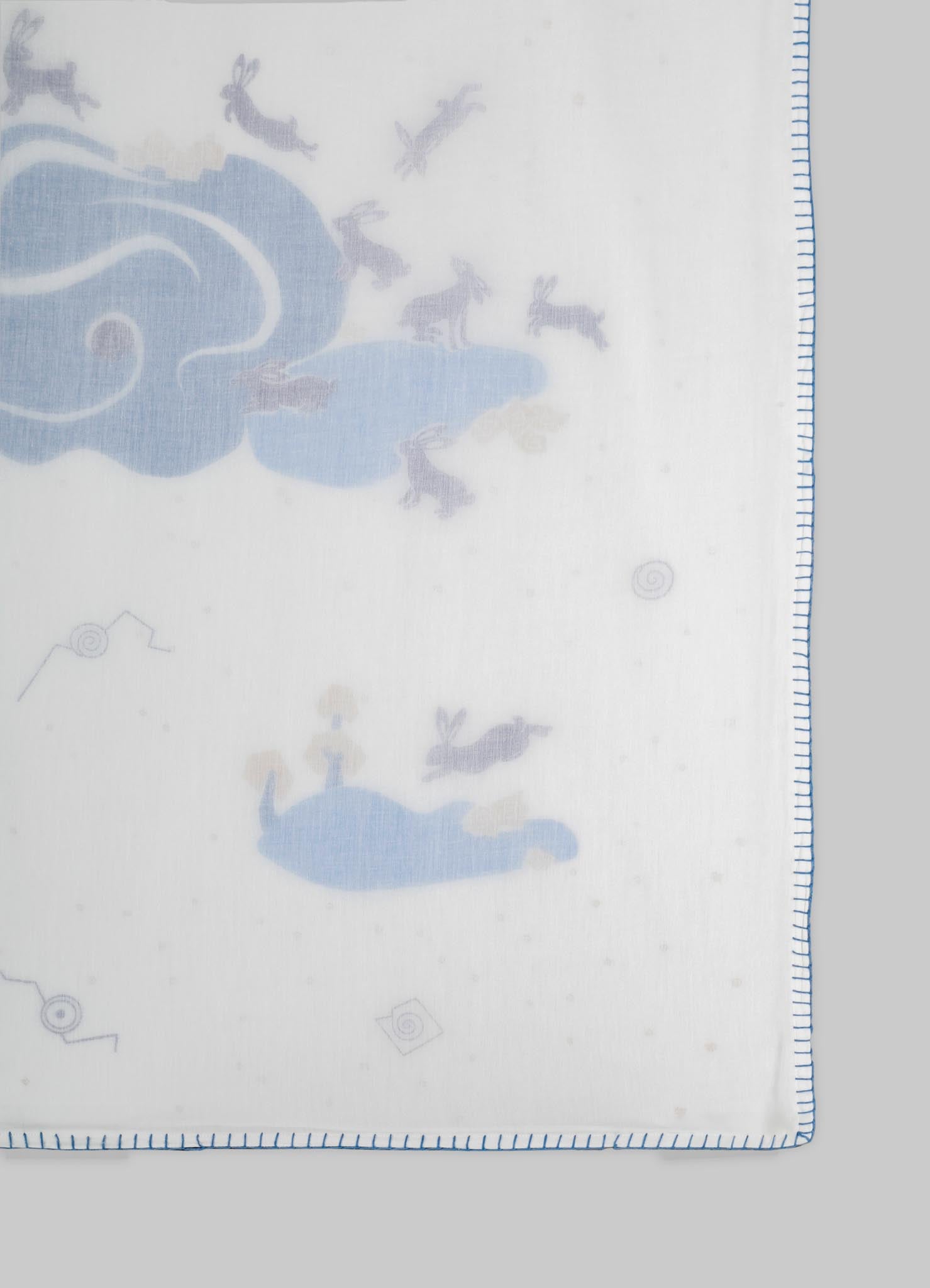 A fabric with a light background featuring a pattern of blue clouds and gray rabbits, bordered by a blue stitch edge. The material appears to be soft and lightweight, likely suitable for textiles or home decor.