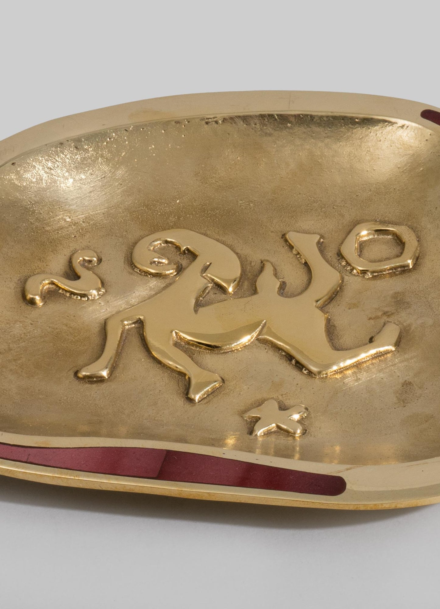 A decorative dish or tray with a gold-colored interior surface and an embossed lion motif, featuring a smooth, curved shape and a metallic finish, set against a light background.