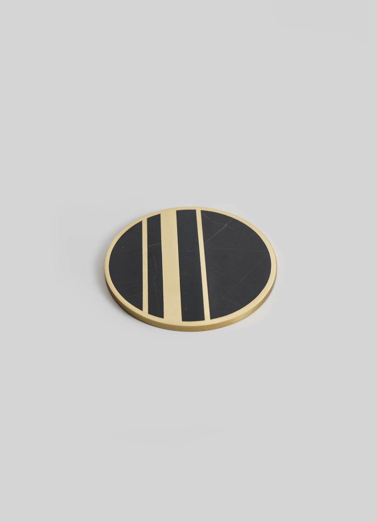 A round coaster with a black marble surface and a beige border, featuring a geometric pattern of beige and black stripes.