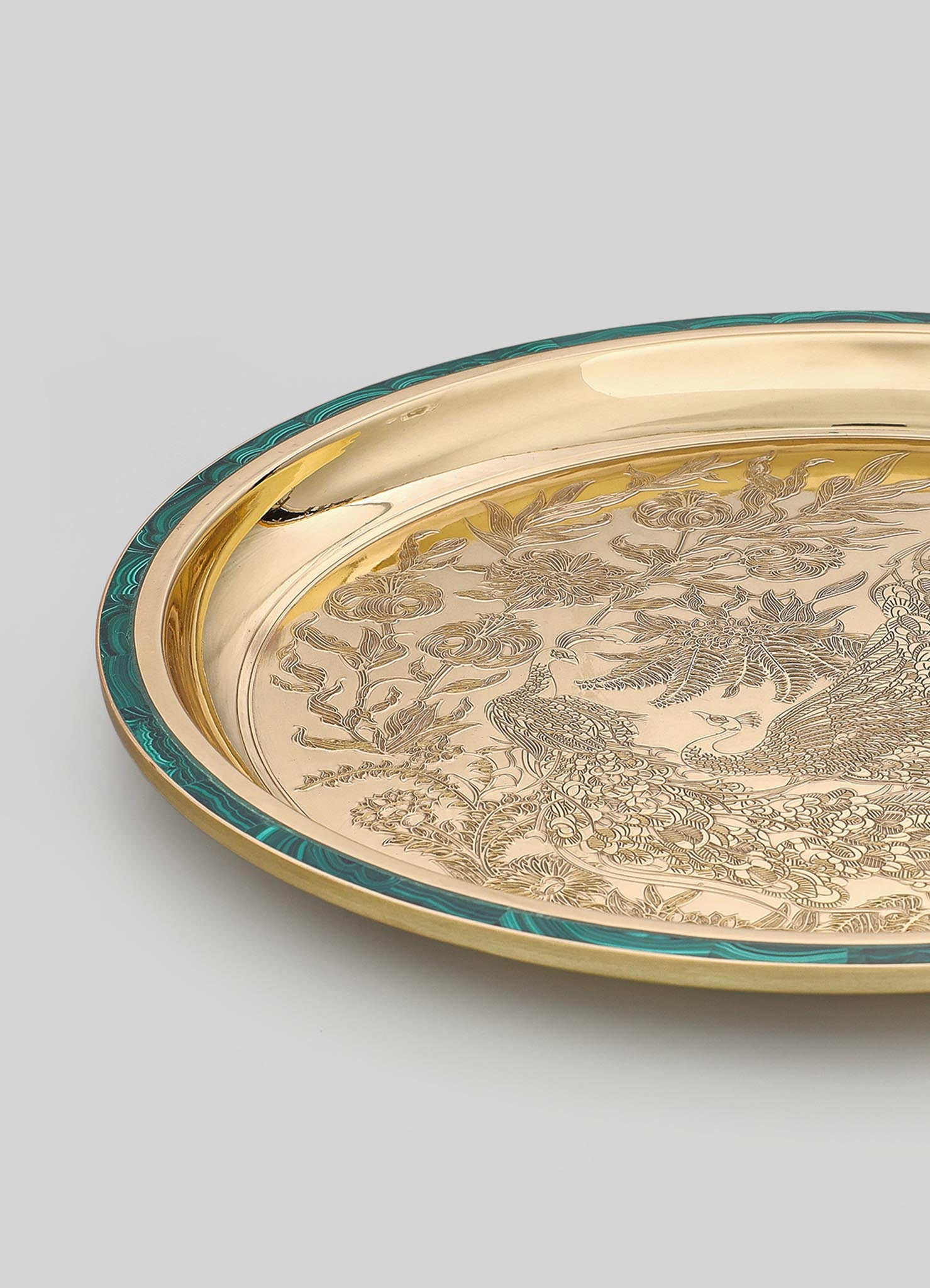 A decorative metal tray featuring intricate engraved motifs of birds and floral patterns, with a polished gold finish and a contrasting teal-colored border.