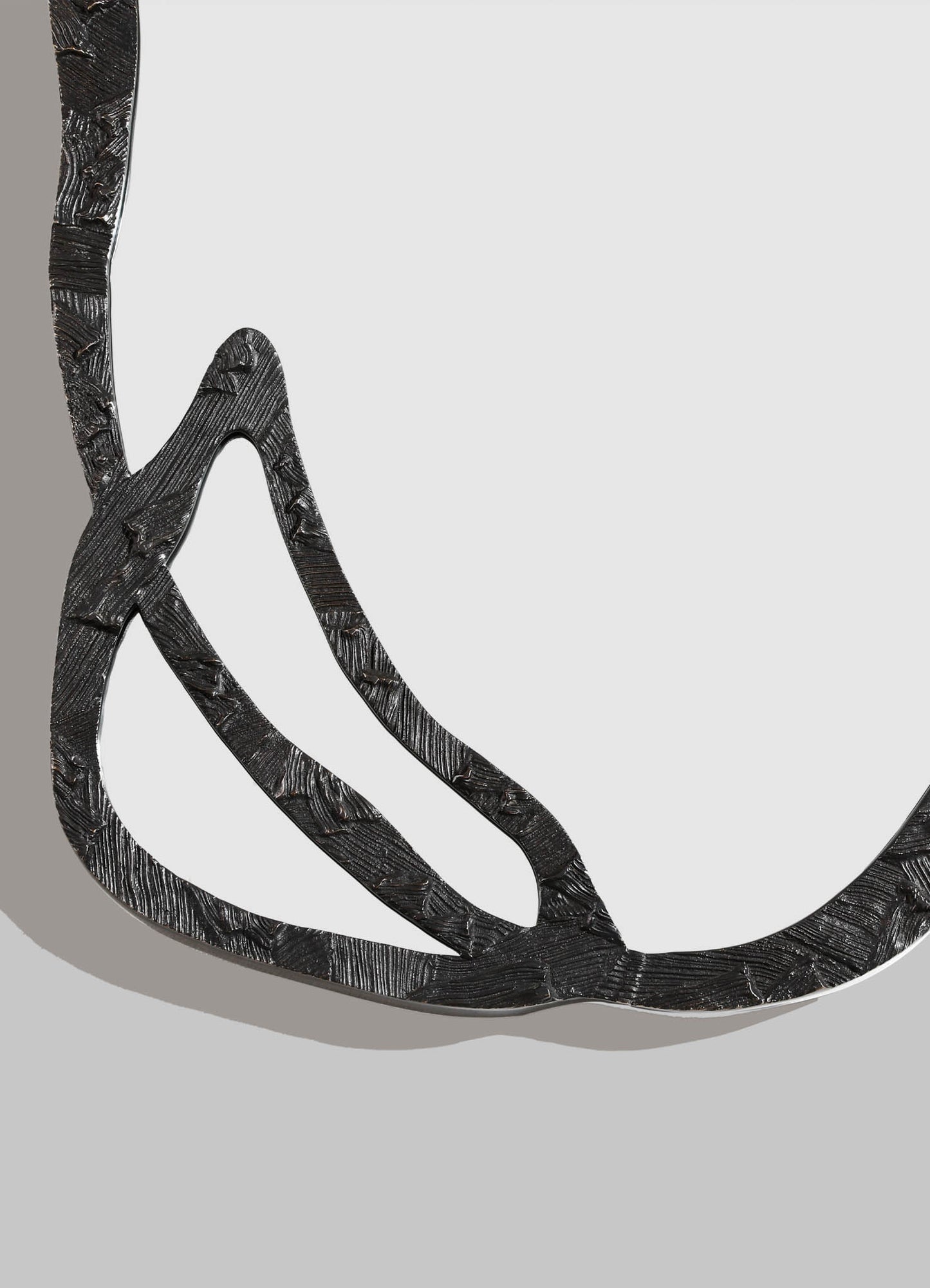 A black metal frame with a textured, carved surface forming a curving, abstract shape. The frame has a matte finish and intricate detailing.