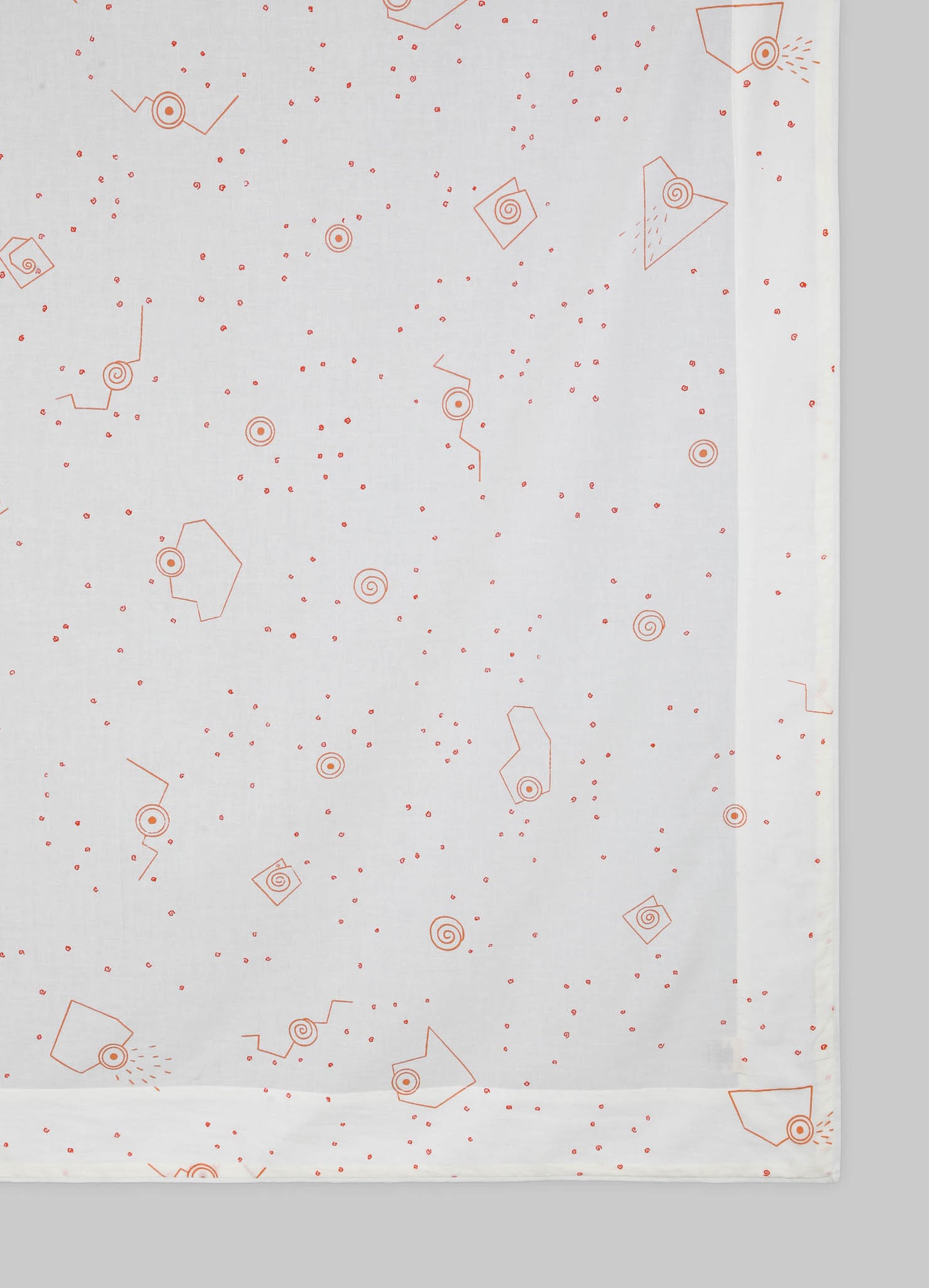 Light-colored tablecloth with a geometric pattern featuring small red spirals and angular shapes, made from a soft fabric.