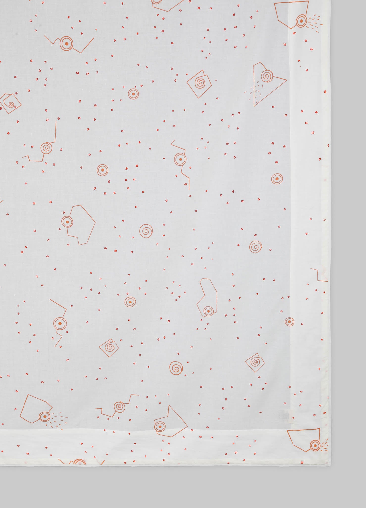 Light-colored tablecloth with a geometric pattern featuring small red spirals and angular shapes, made from a soft fabric.