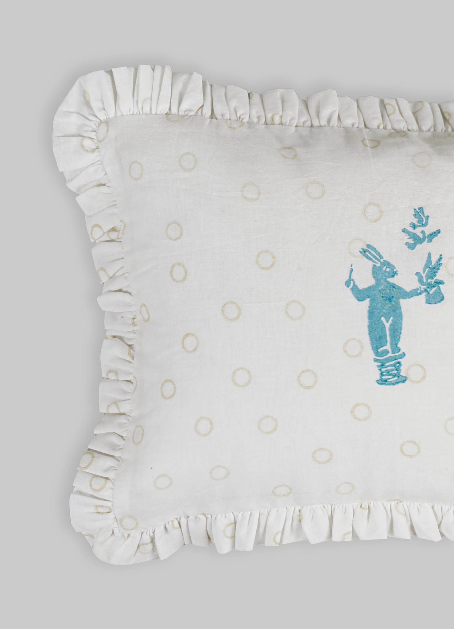 White embroidered cushion cover with ruffled edges, featuring a blue embroidered rabbit motif and a pattern of beige circles on a soft fabric background.