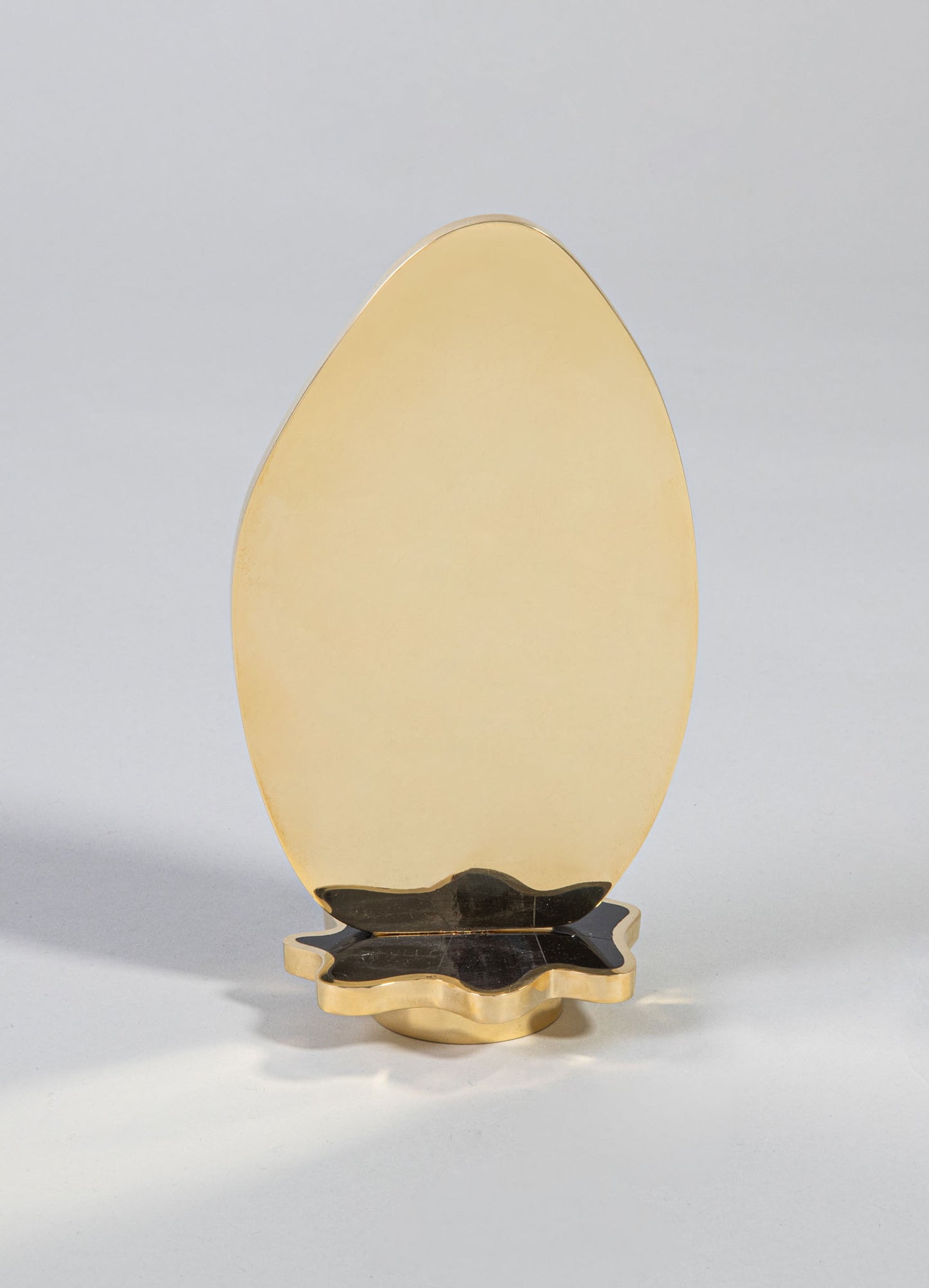 A decorative table mirror with an oval shape featuring a gold-colored frame and a matching scalloped black and gold base, exhibiting a luxurious and vintage style.