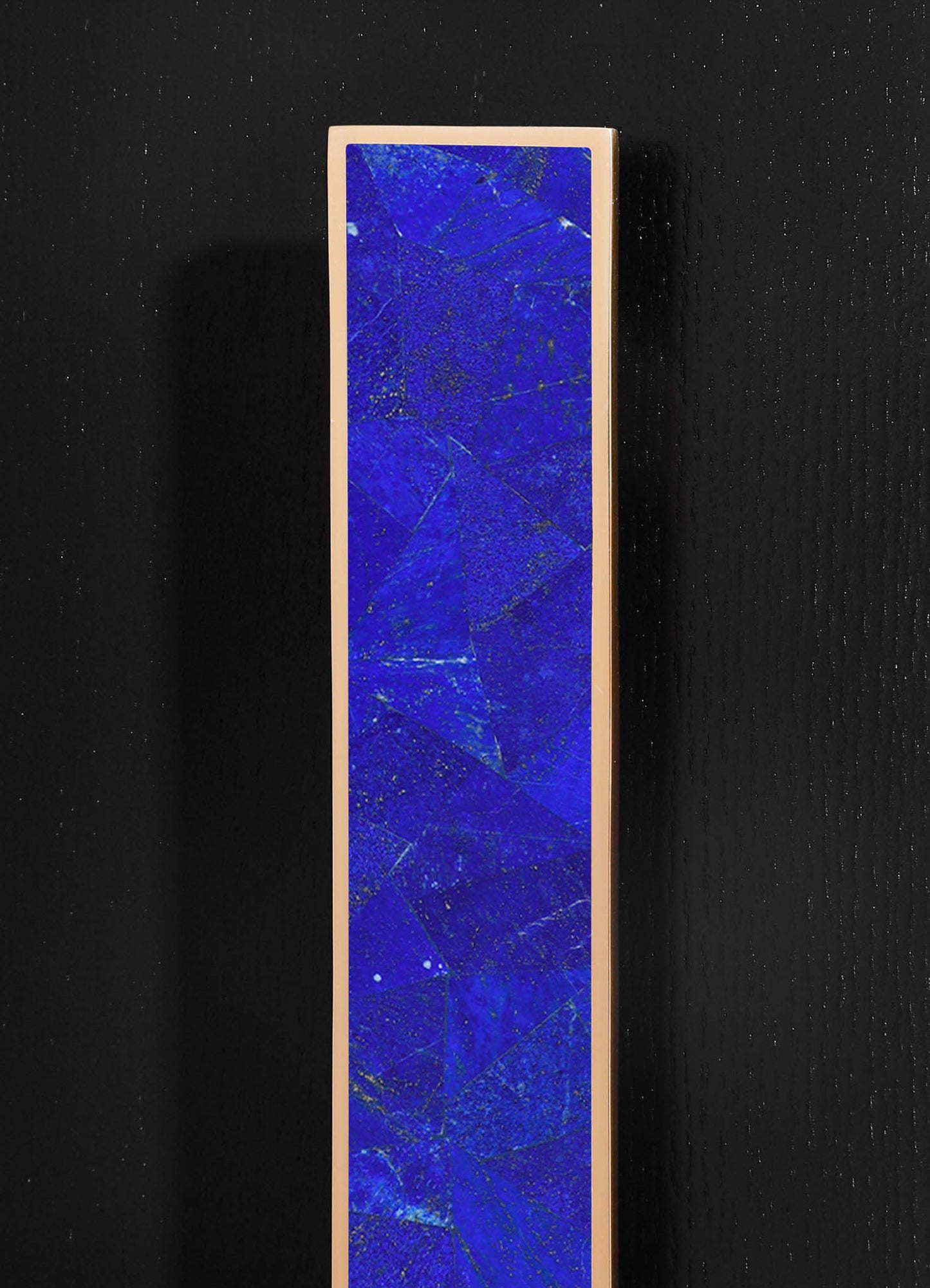 A tall, rectangular artwork featuring a vivid blue surface with gold flecks and fine crackle details, framed by a slim, neutral-colored border. The piece has a contemporary style with an abstract motif, displayed against a black textured background.