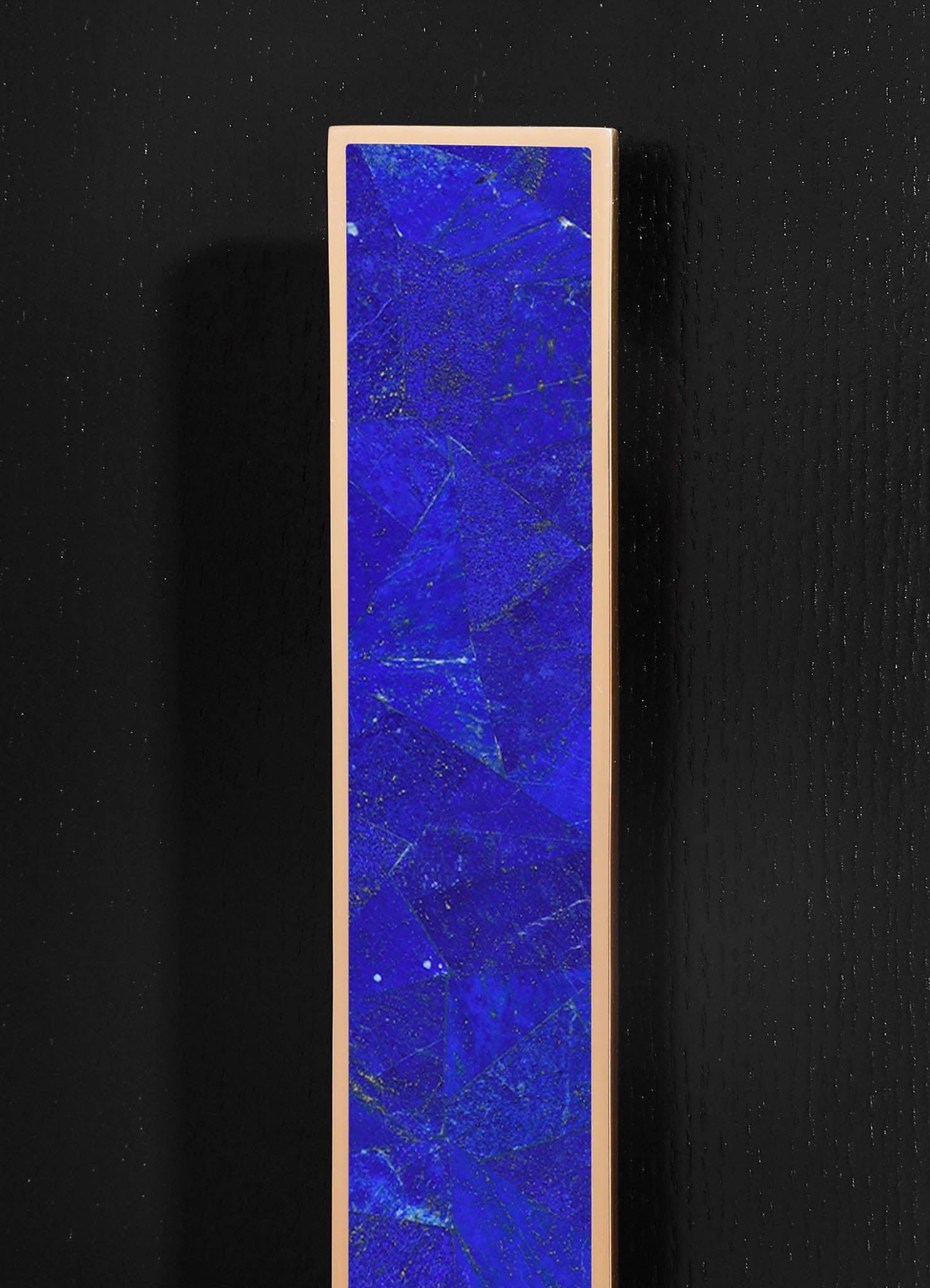 A tall, rectangular artwork featuring a vivid blue surface with gold flecks and fine crackle details, framed by a slim, neutral-colored border. The piece has a contemporary style with an abstract motif, displayed against a black textured background.