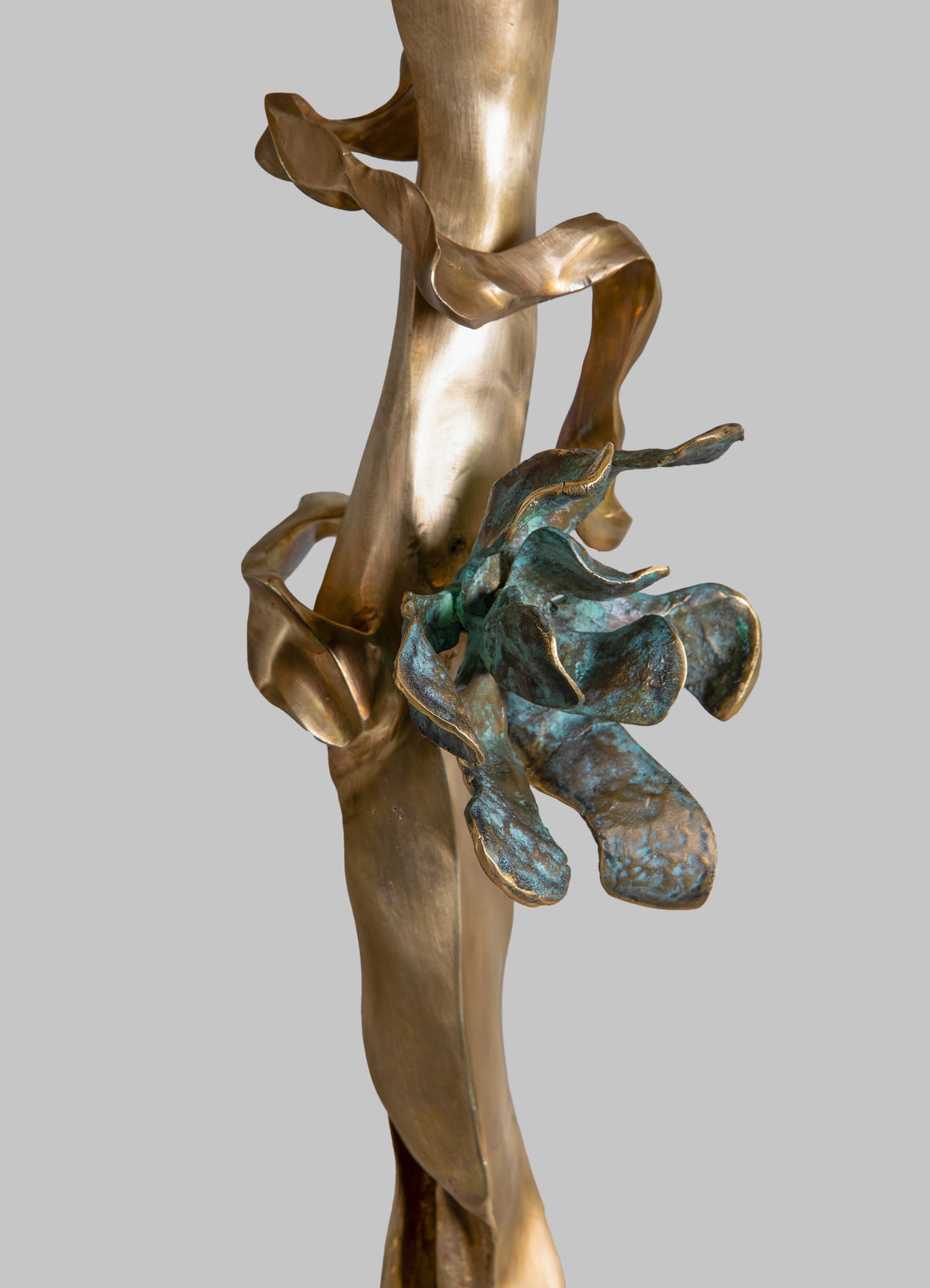A sculptural artwork made of metal with a combination of brass and patinated elements, featuring organic, leaf-like shapes and flowing, curvilinear forms, set against a plain background. The piece emphasizes natural motifs and a handcrafted, abstract design style.