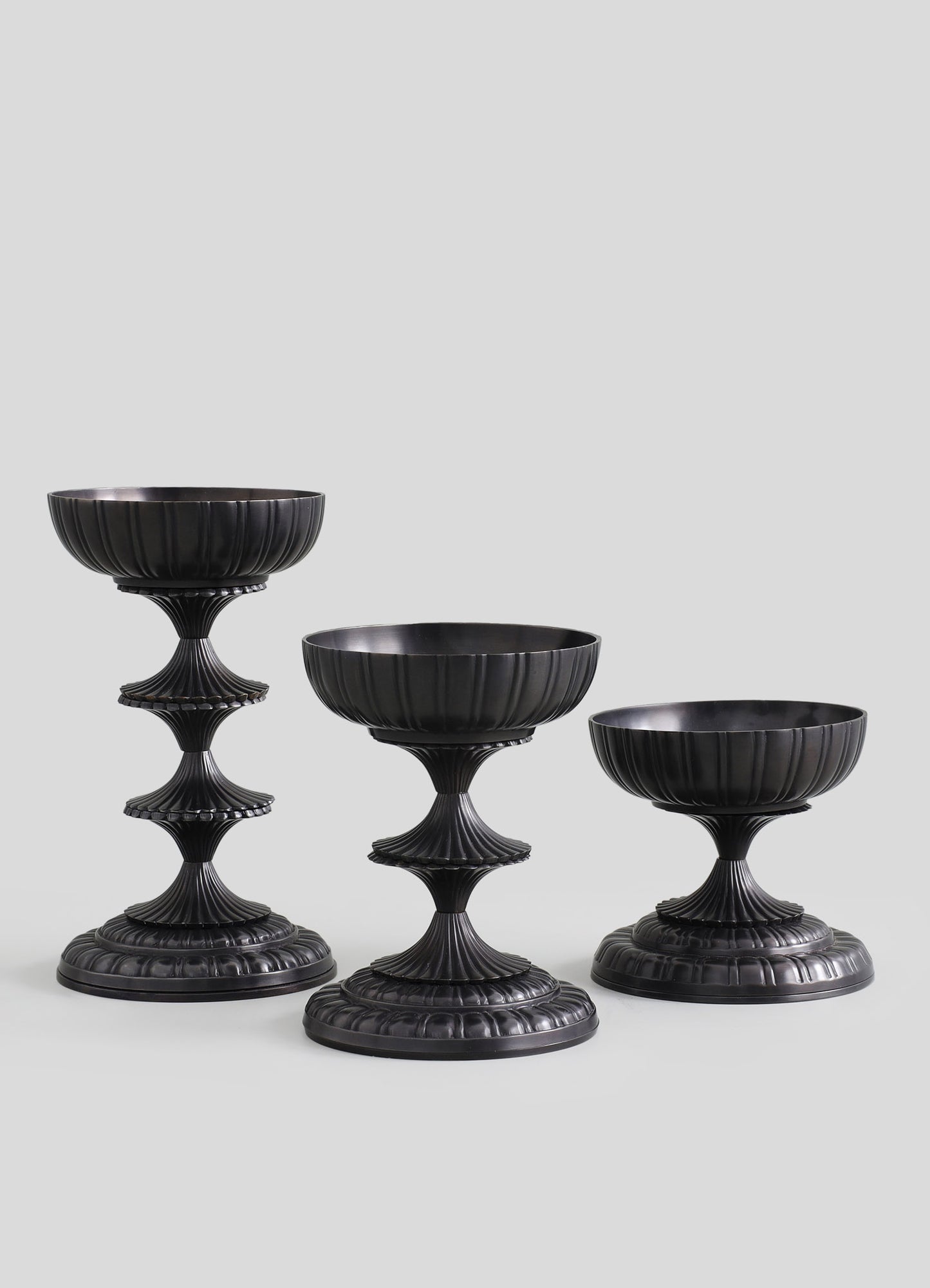 Set of three black ceramic or resin pedestals with vertical ribbed patterns, featuring fluted, tiered bases and rounded bowls on top, designed for display or decorative purposes.