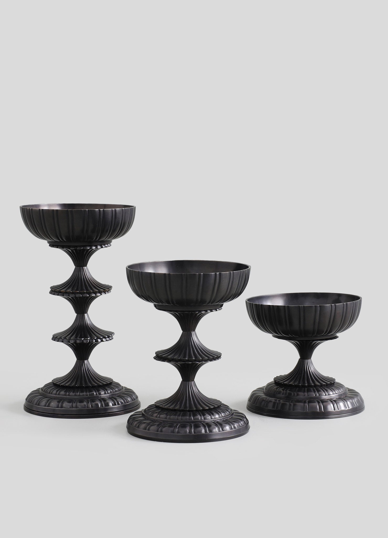 Set of three black ceramic or resin pedestals with vertical ribbed patterns, featuring fluted, tiered bases and rounded bowls on top, designed for display or decorative purposes.