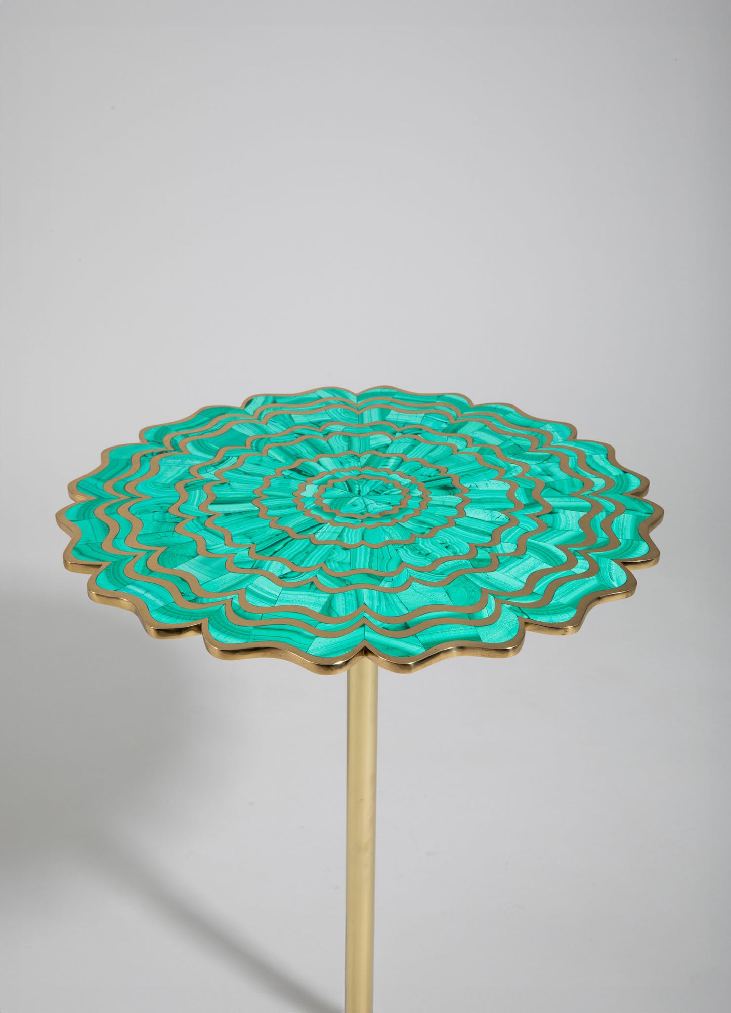 A decorative side table featuring a circular top with a layered, wavy pattern in shades of turquoise and gold accents, supported by a slender gold-colored metal stand. The design has a handcrafted, modern style with vibrant colors.