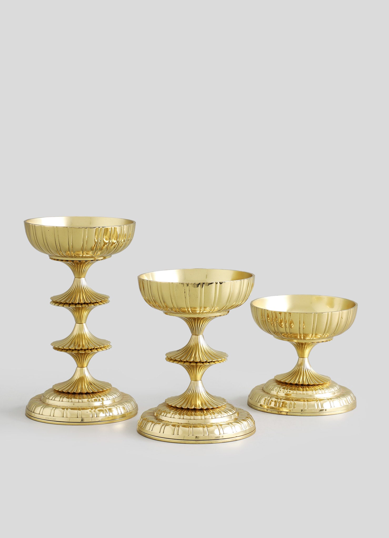 Set of three gold-colored decorative bowls with scalloped edges and fluted, tiered bases, made of metal with a shiny finish, arranged on a plain background.