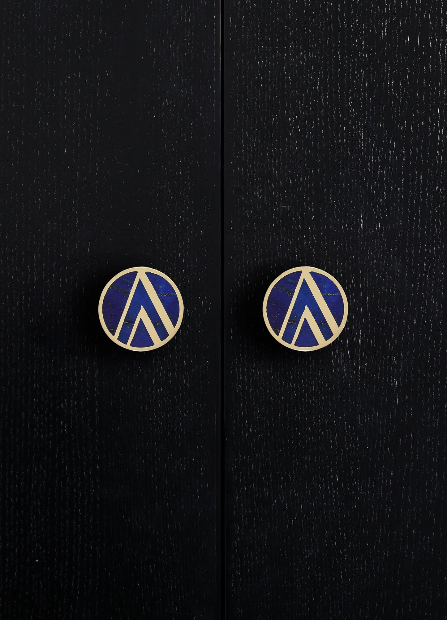 Black wooden surface with a textured finish, featuring two round handles with blue and gold geometric pattern and metallic gold edges.