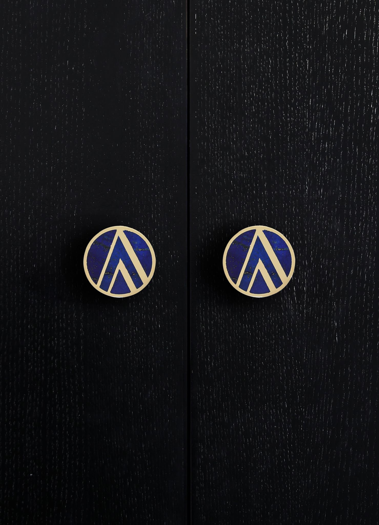 Black wooden surface with a textured finish, featuring two round handles with blue and gold geometric pattern and metallic gold edges.