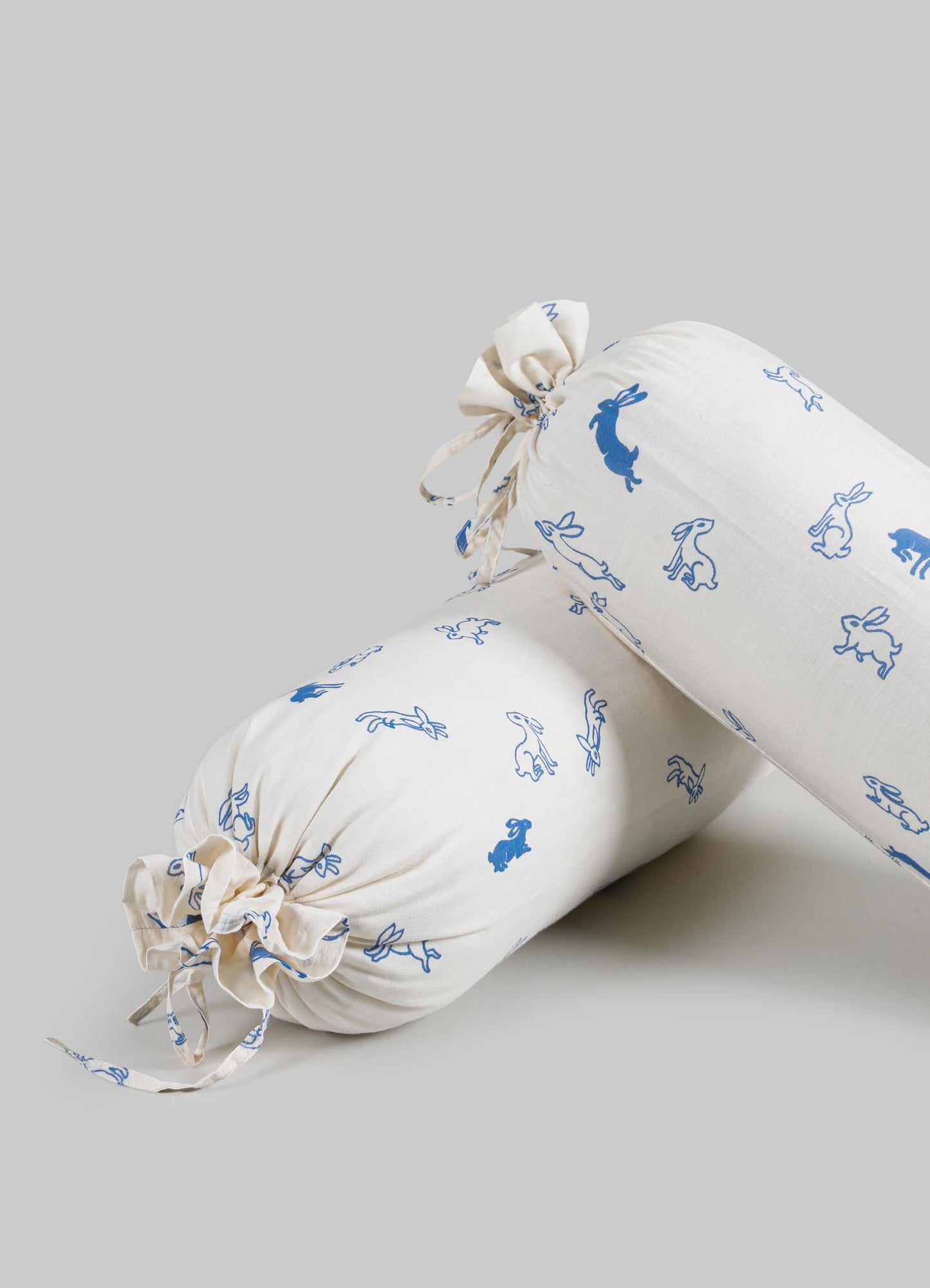 Cream-colored fabric bolster pillows with blue rabbit print pattern, featuring tied fabric ends and a soft, lightweight material.