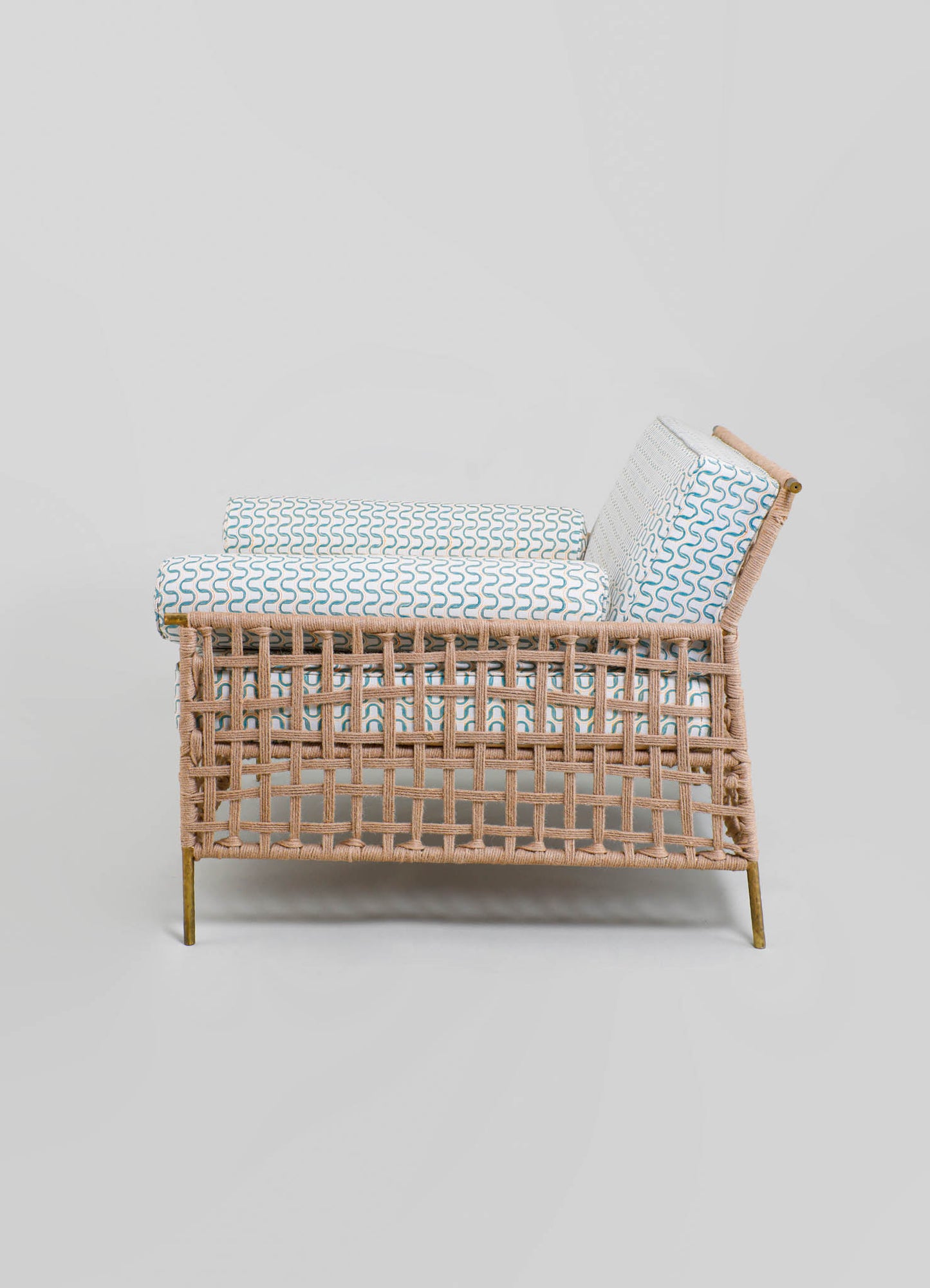 Wicker lounge chair with a natural finish, featuring a slatted design and slender brass legs. It is upholstered with cushions and a backrest in white fabric with blue geometric wave patterns.