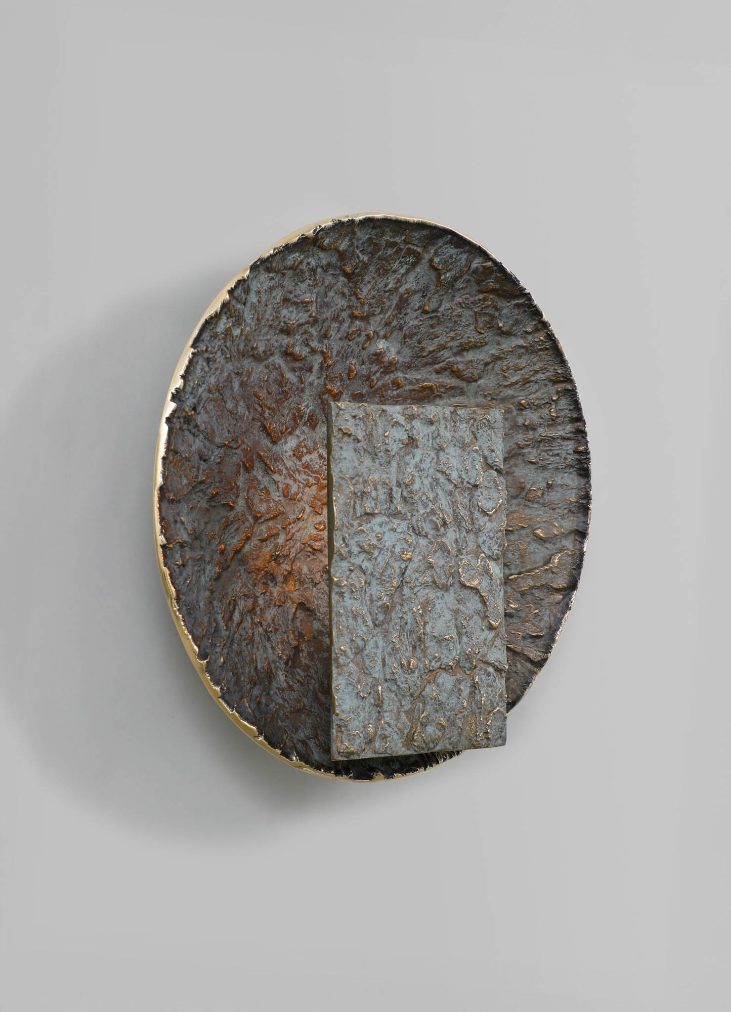 A round sculpture or decorative object with a textured, rusted metal surface in dark reddish-brown tones, with a rectangular metal insert of a similar texture and color.