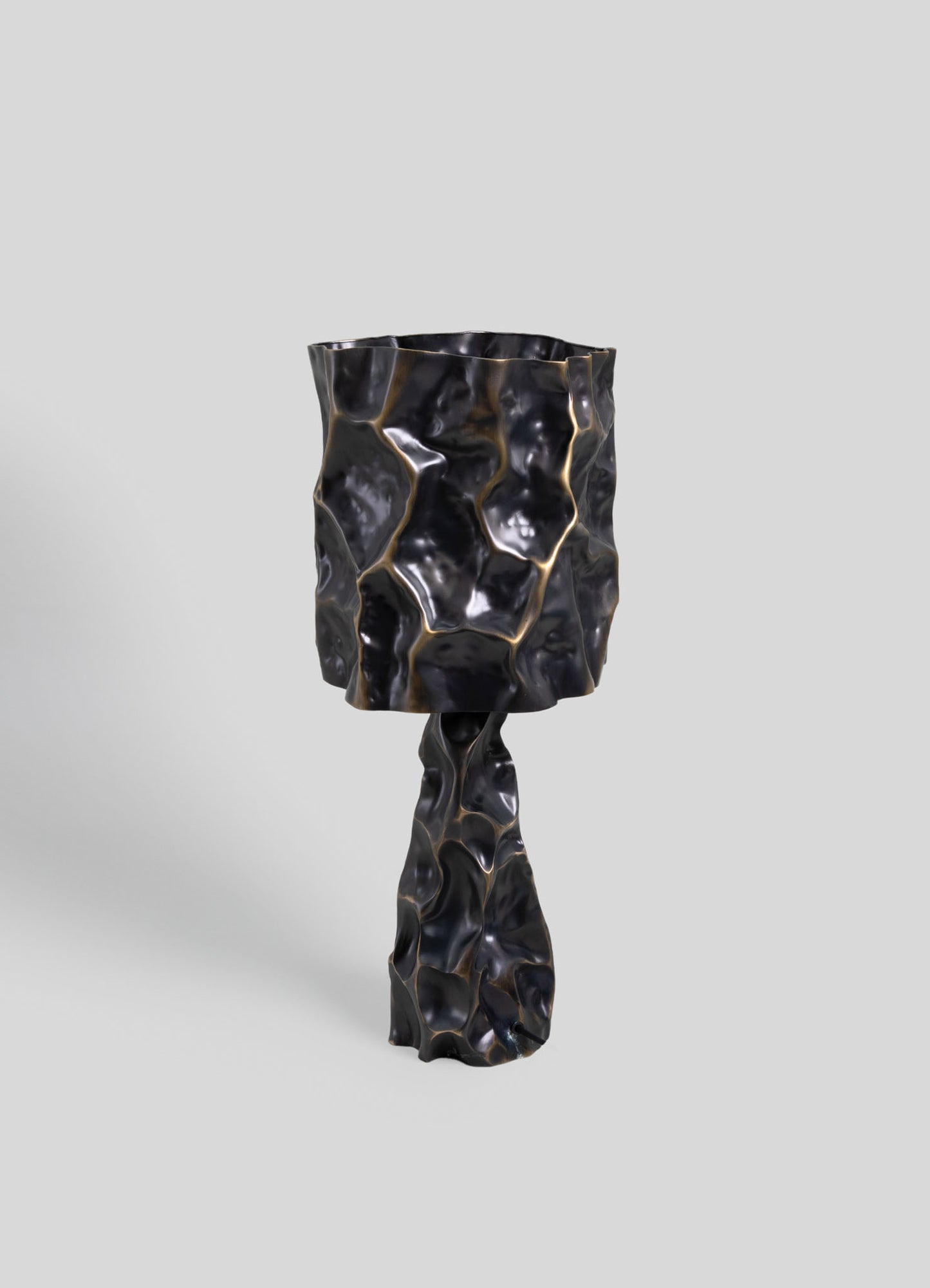A sculptural side table or accent piece with a textured, crumpled appearance in black resin or lacquer with gold accents, featuring an irregular, organic form and a glossy finish.
