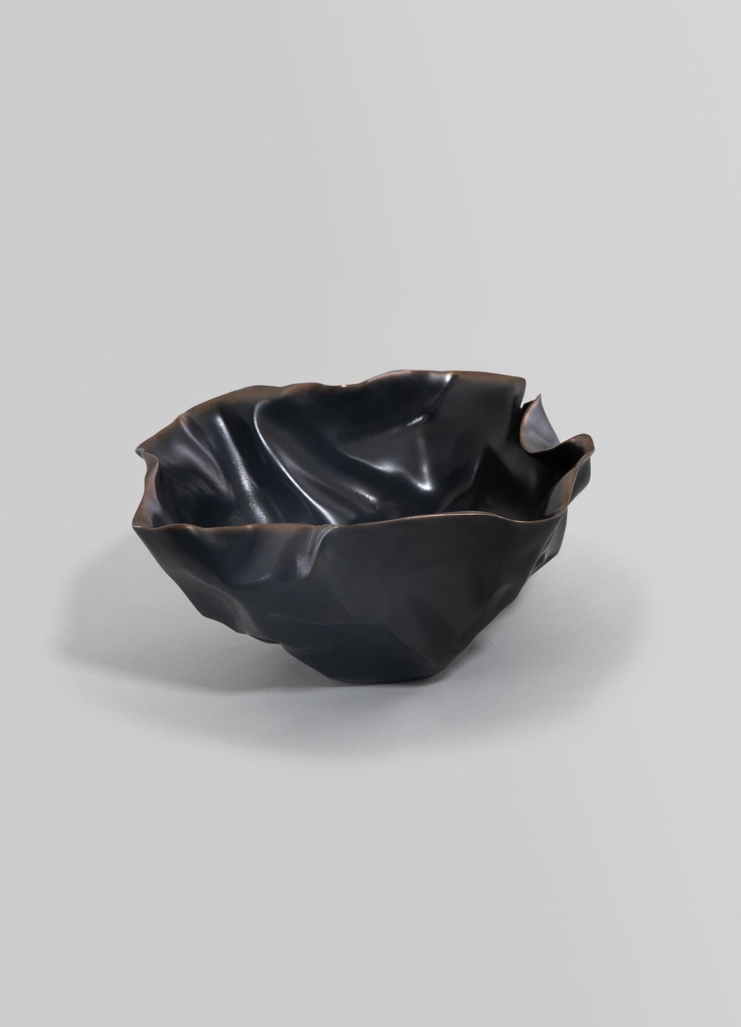 Handcrafted black ceramic bowl with an irregular, crumpled appearance and a glossy finish, presented against a plain background.
