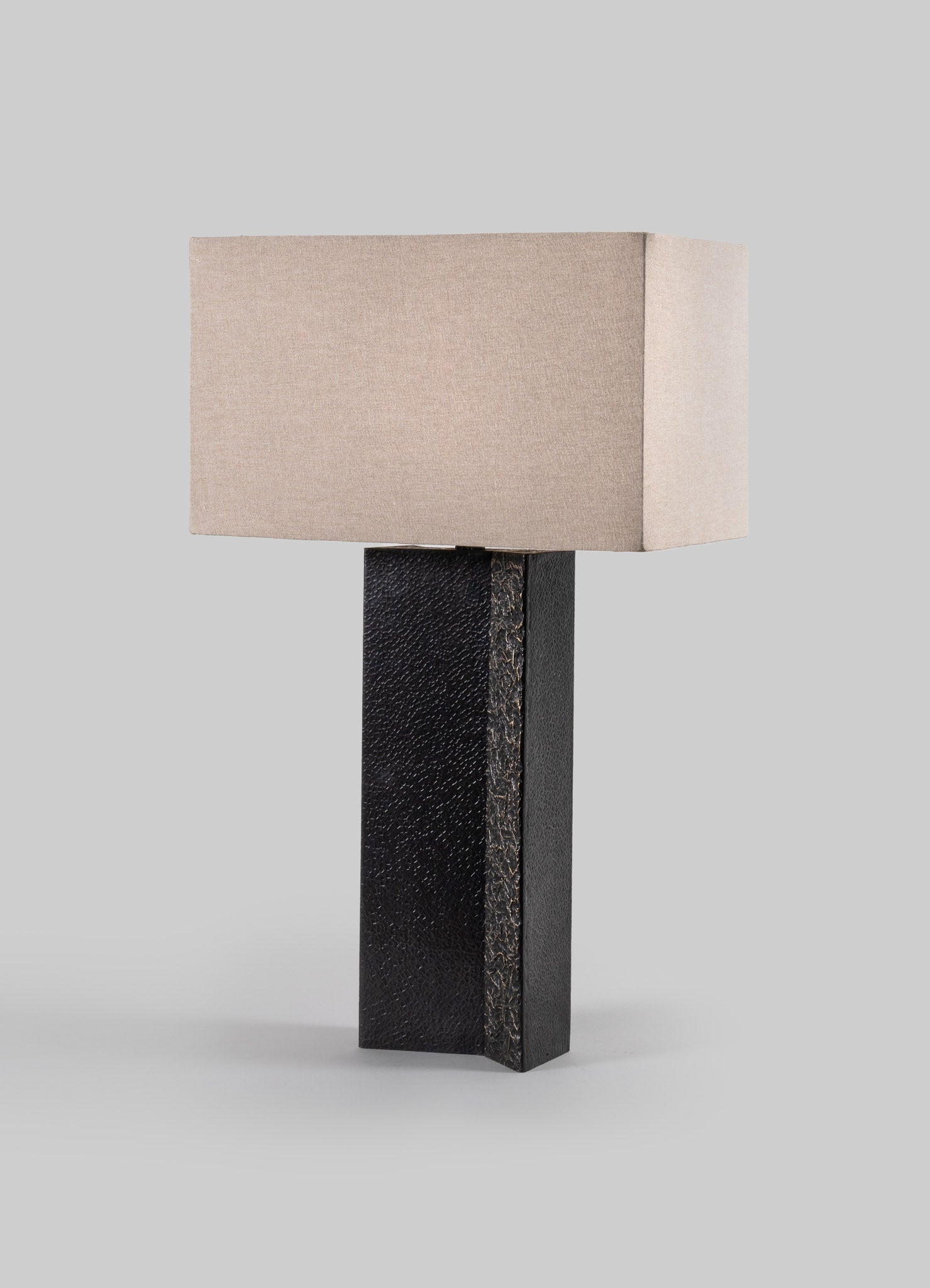 Table lamp with a rectangular beige fabric shade and a textured black rectangular base, combining modern and minimalist style.