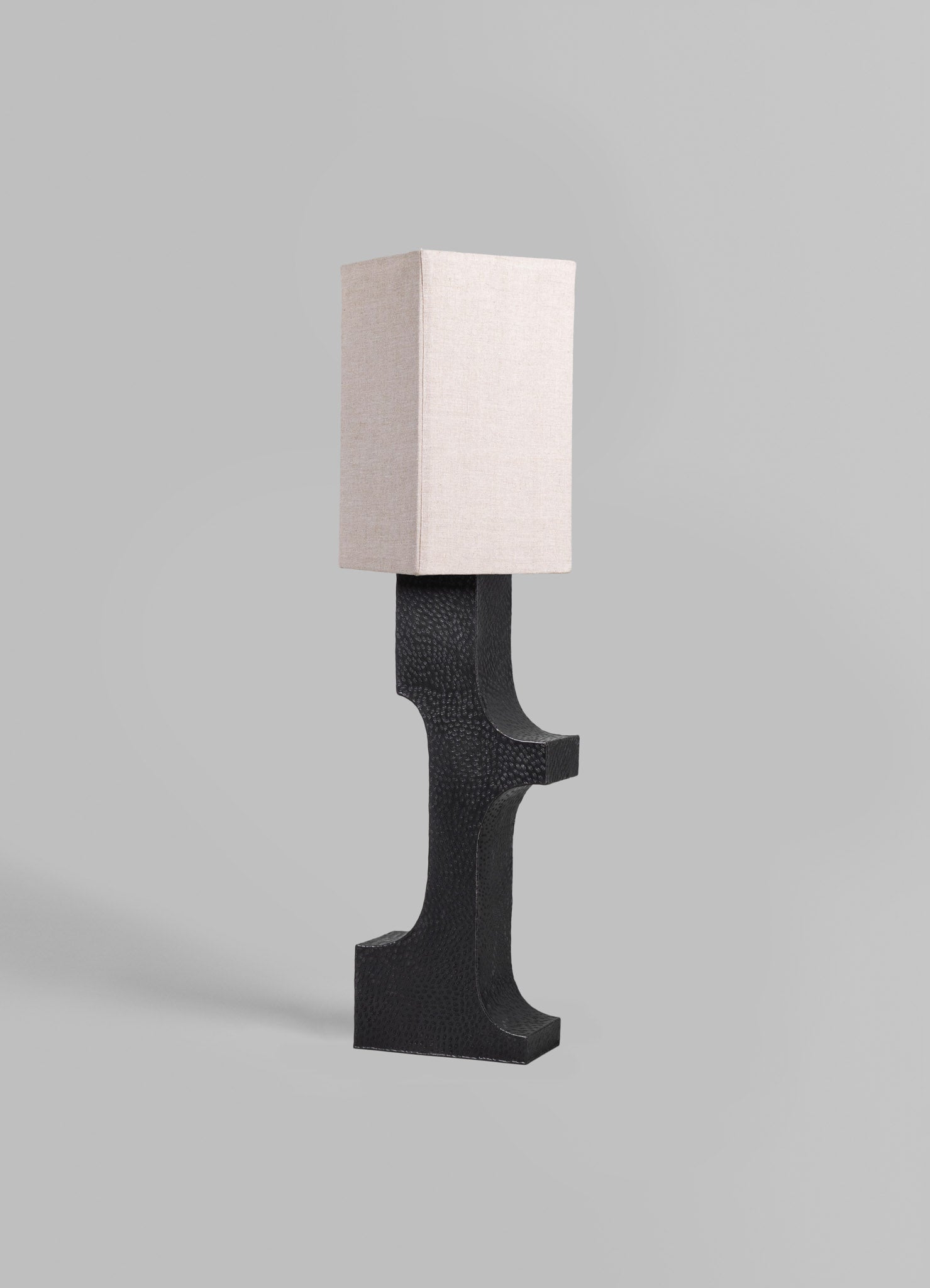 A table lamp with a textured black base and a rectangular fabric lampshade in a neutral beige tone, set against a plain background.