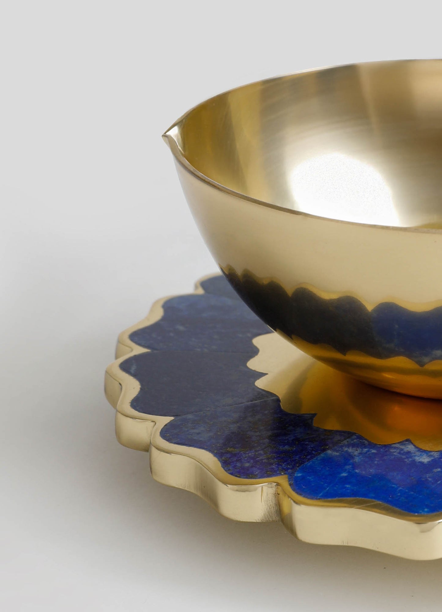 A metallic gold and black ceramic bowl with a smooth, shiny finish, placed on a decorative scalloped-edge tray with blue and gold accents. The setting suggests a contemporary style with a luxurious and artistic feel.