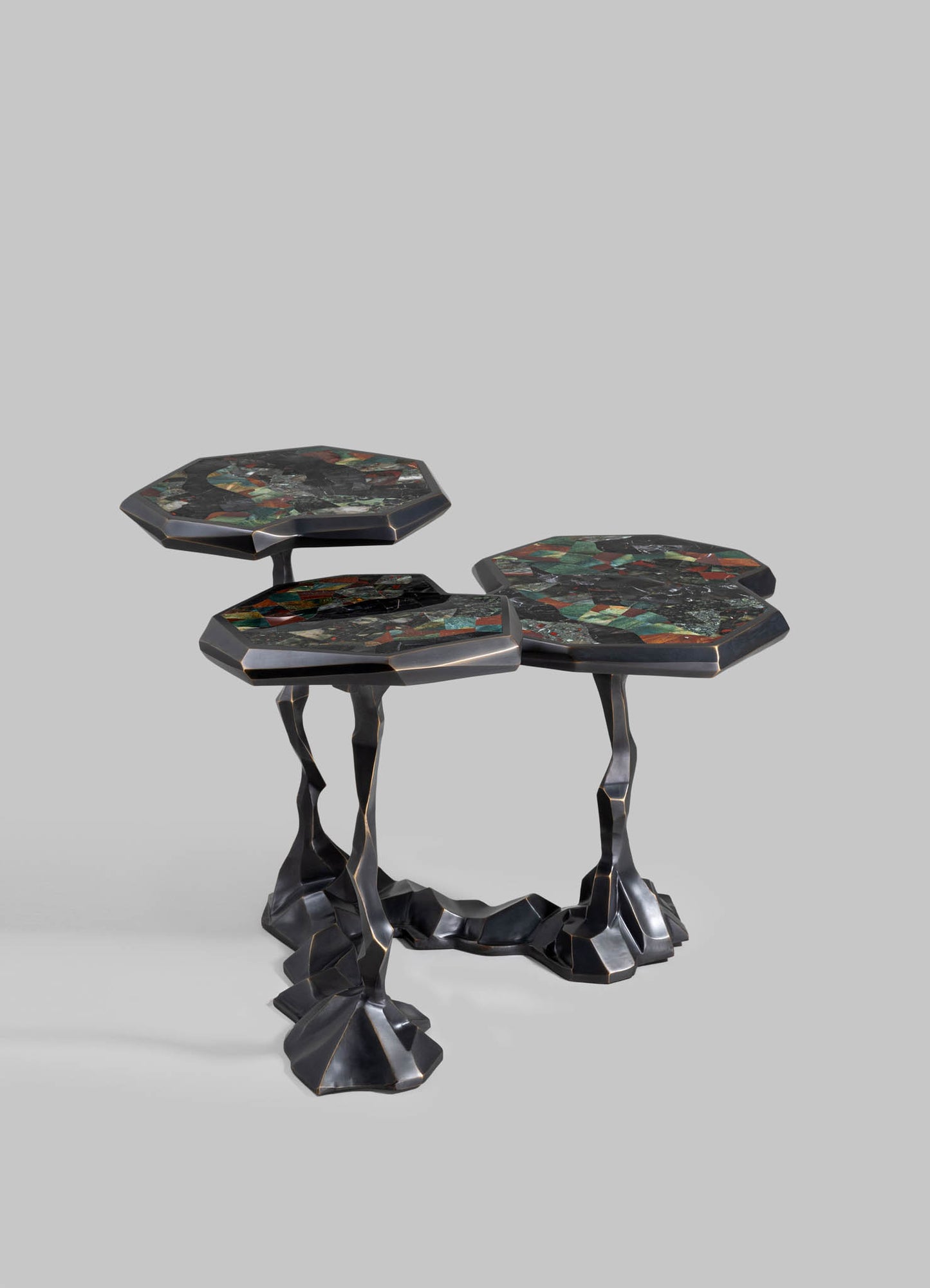 A set of three nesting side tables with irregular, sculptural metal bases in a dark finish and tabletops featuring colorful mosaic patterns in shades of green, red, black, and metallic accents.
